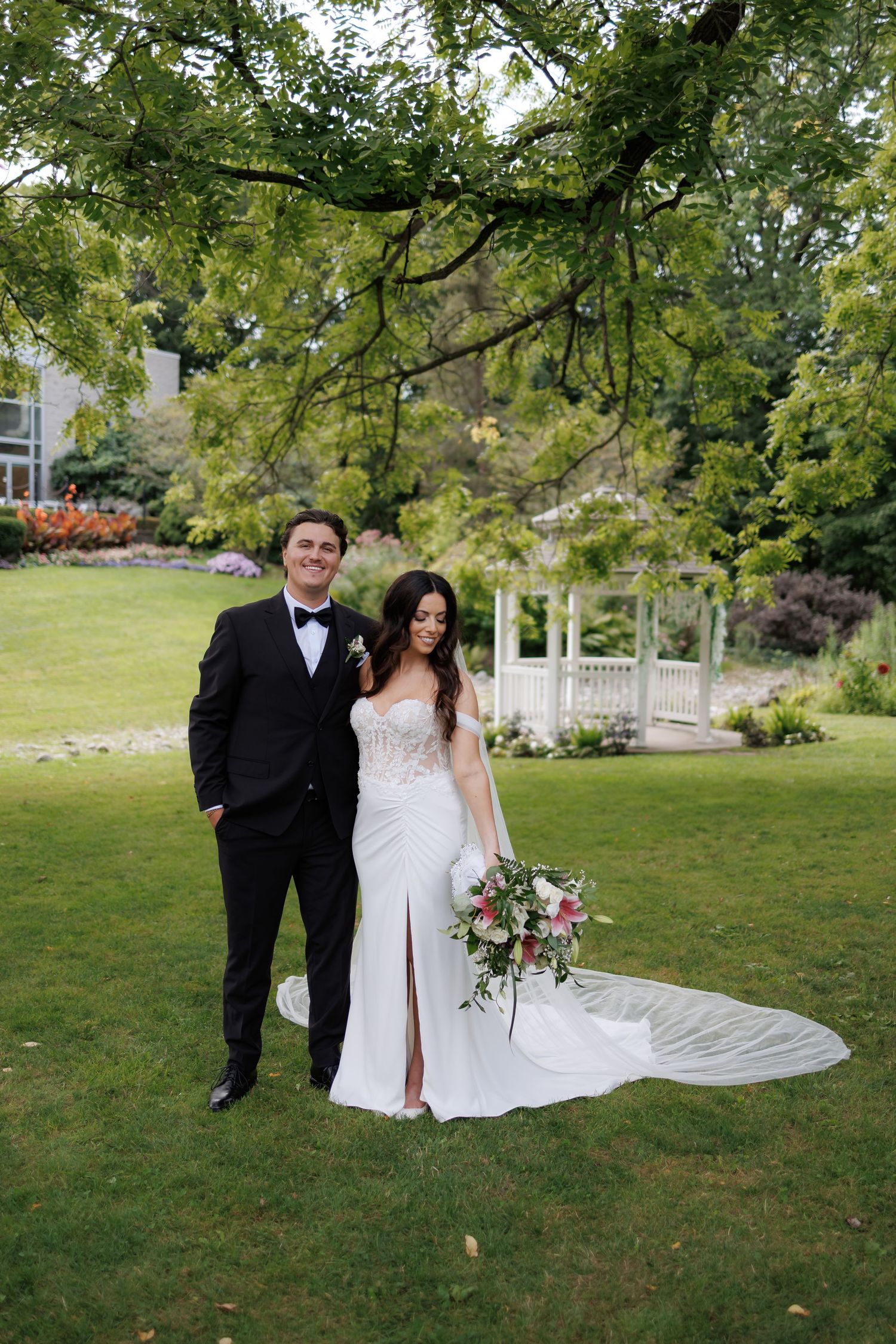 Wedding couple poses in a lush garden setting with a flowing white dress and classic tuxedo.