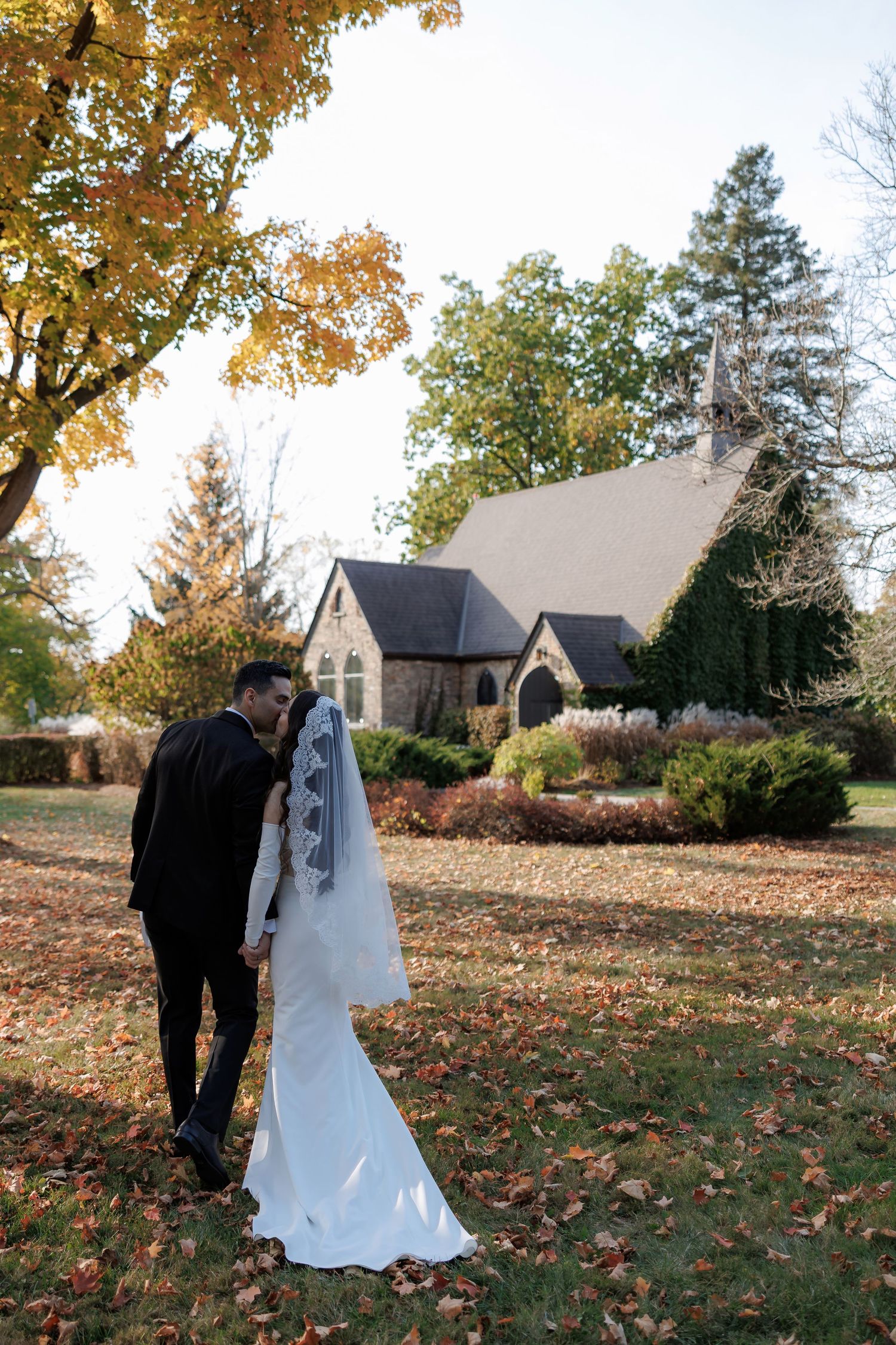 Wedding couple poses in front of historic stone church during golden autumn afternoon.