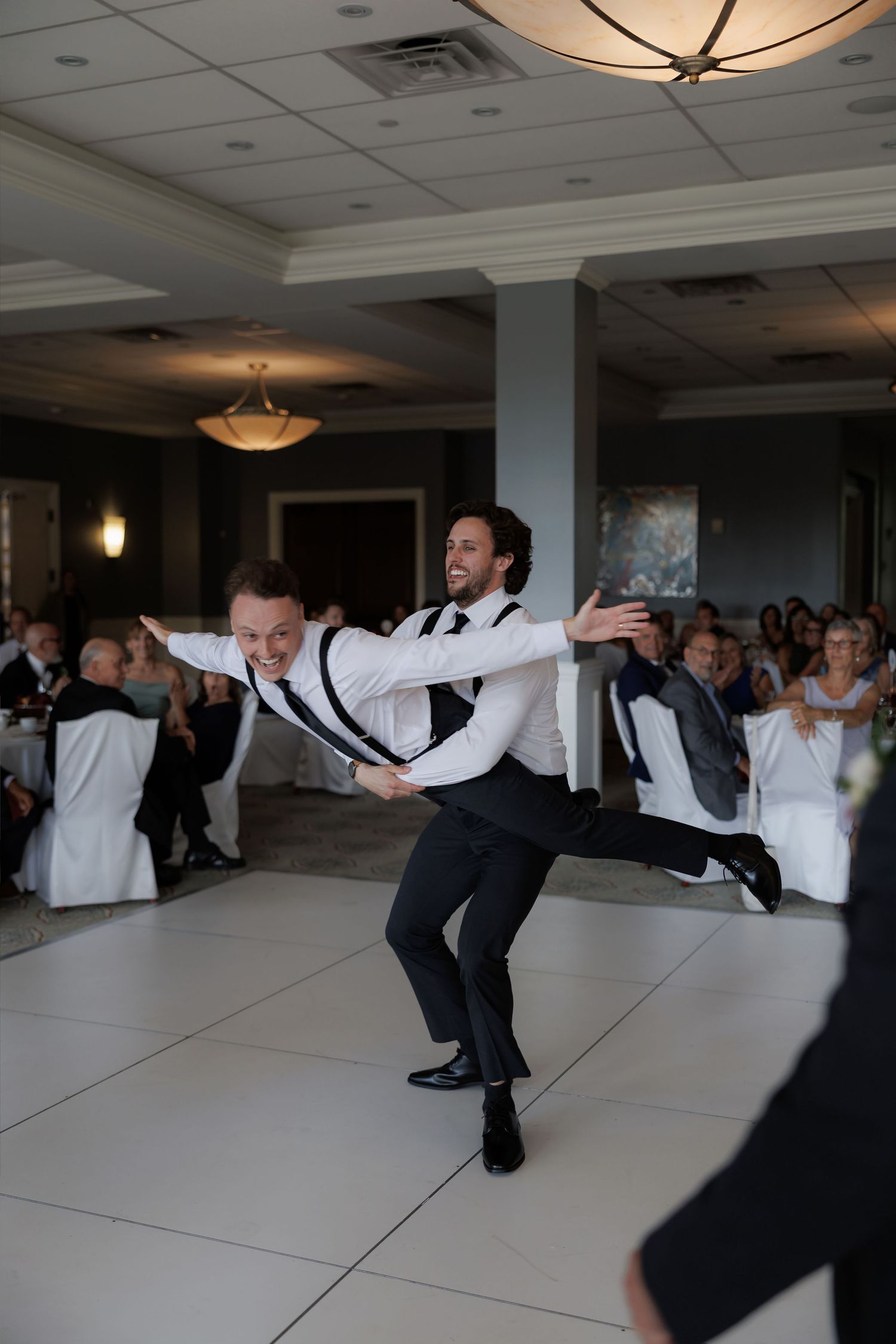 Two groomsmen perform an energetic surprise dance routine on the white wedding reception dance floor.