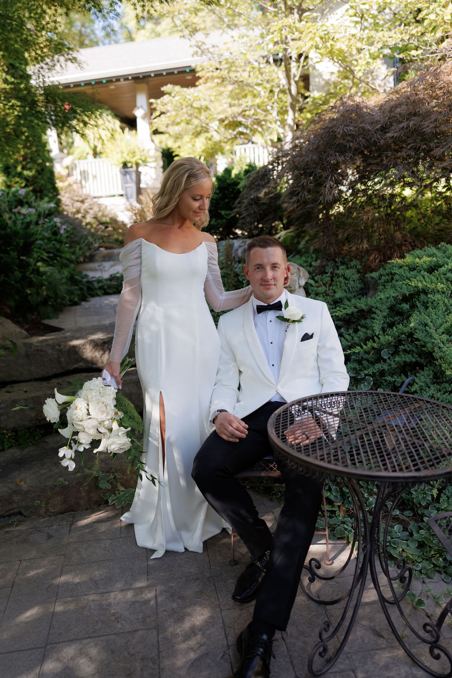 Elegant garden wedding photos with couple seated at wrought iron patio furniture.
