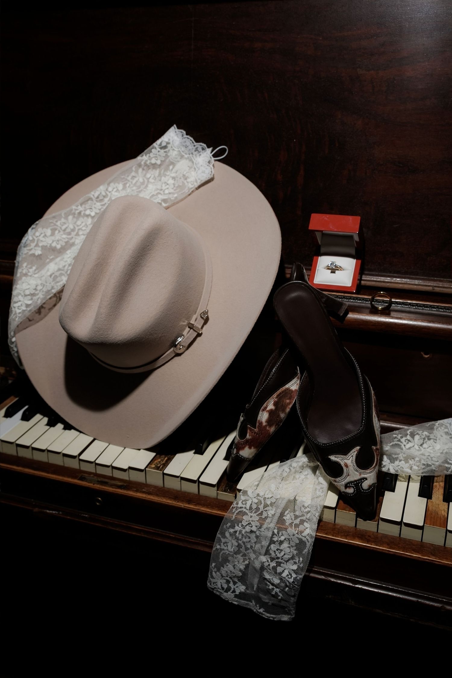 Cowboy hat, cowboy boots, lace veil, and ring box arranged on piano keys for a country western wedding.