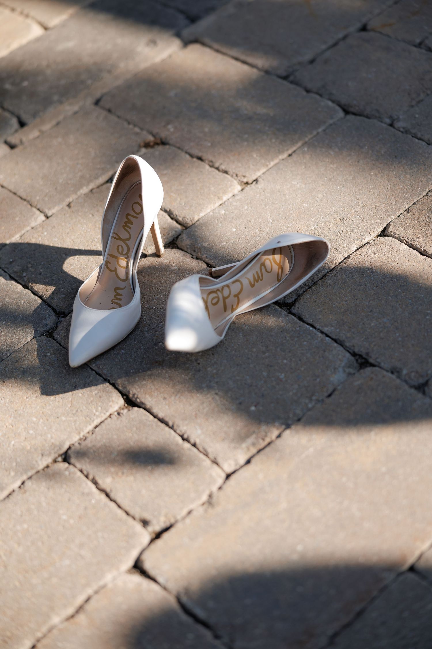 White bridal heels placed on stone pavers with dappled sunlight.