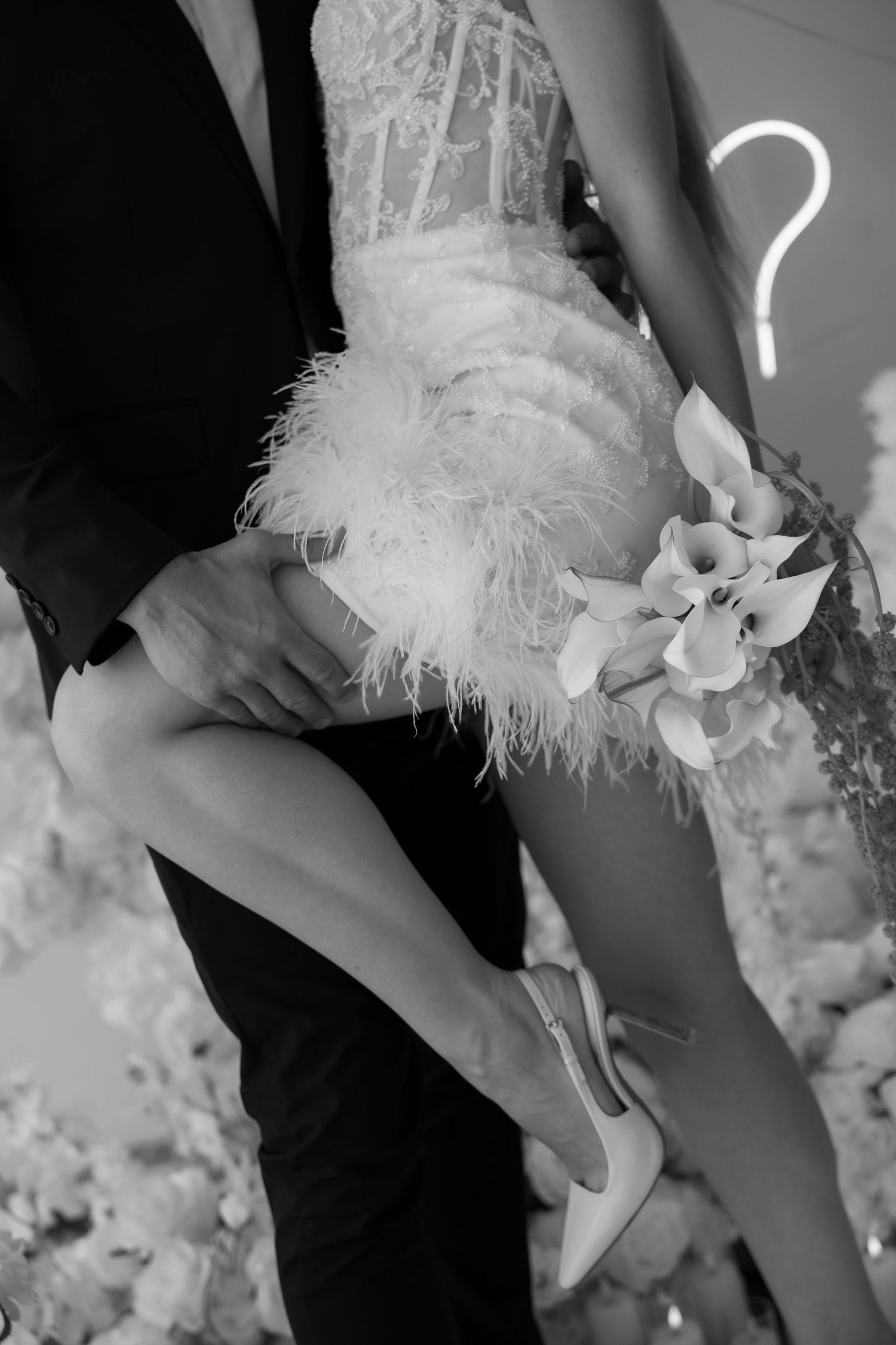 A close-up of a feathered white wedding dress and high heel being adjusted.