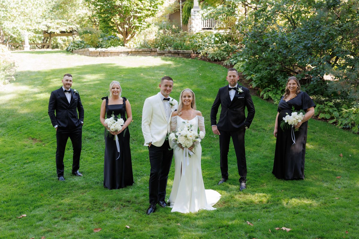 Wedding party members arranged in formal line on grass with trees behind.