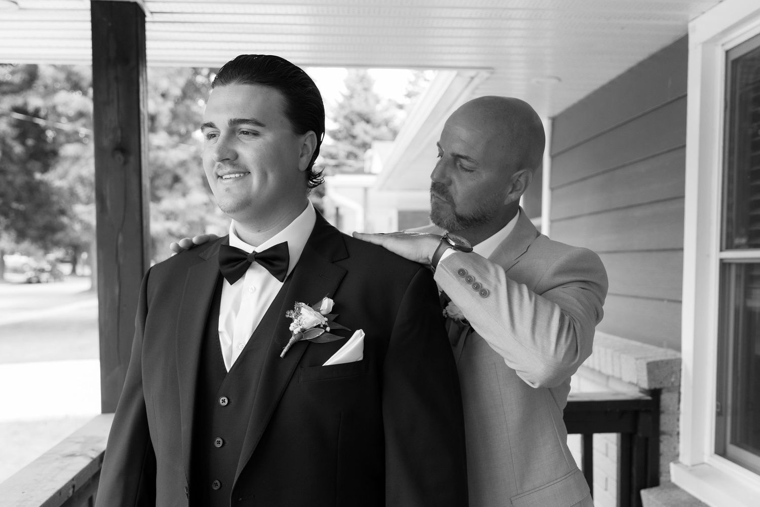 Wedding party members adjusting formal attire on outdoor porch.