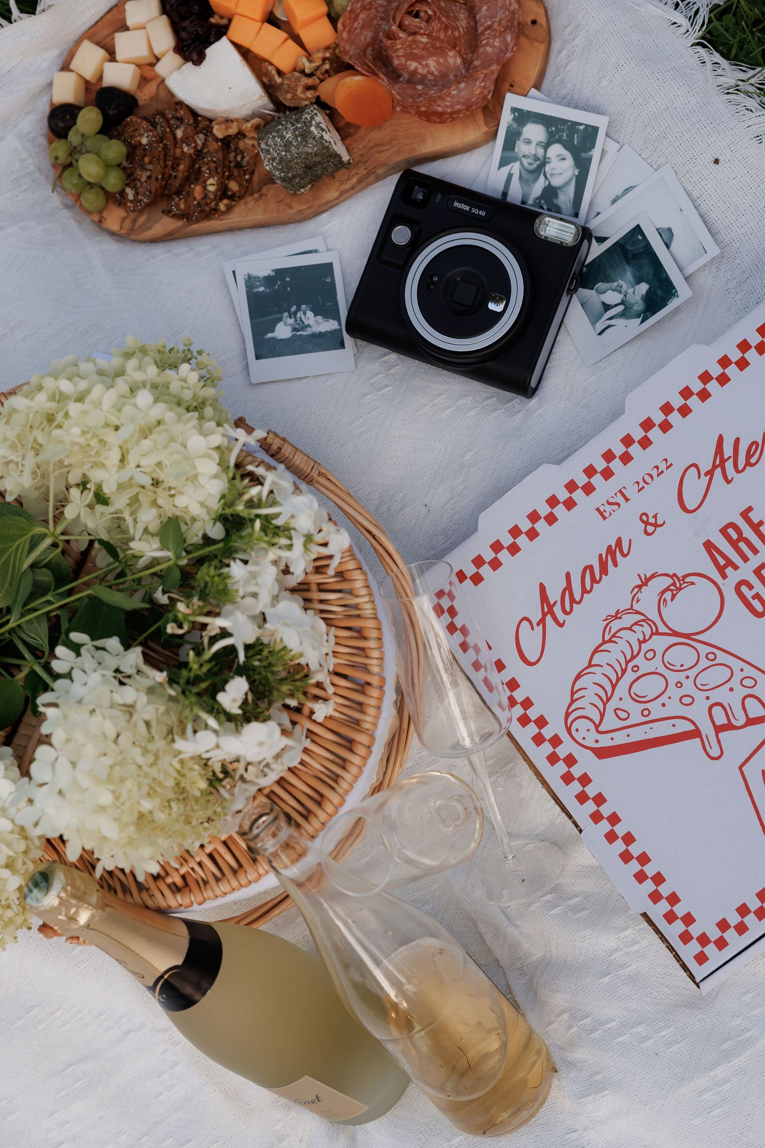 Picnic setup with vintage camera, flowers, and snacks on checkered paper.