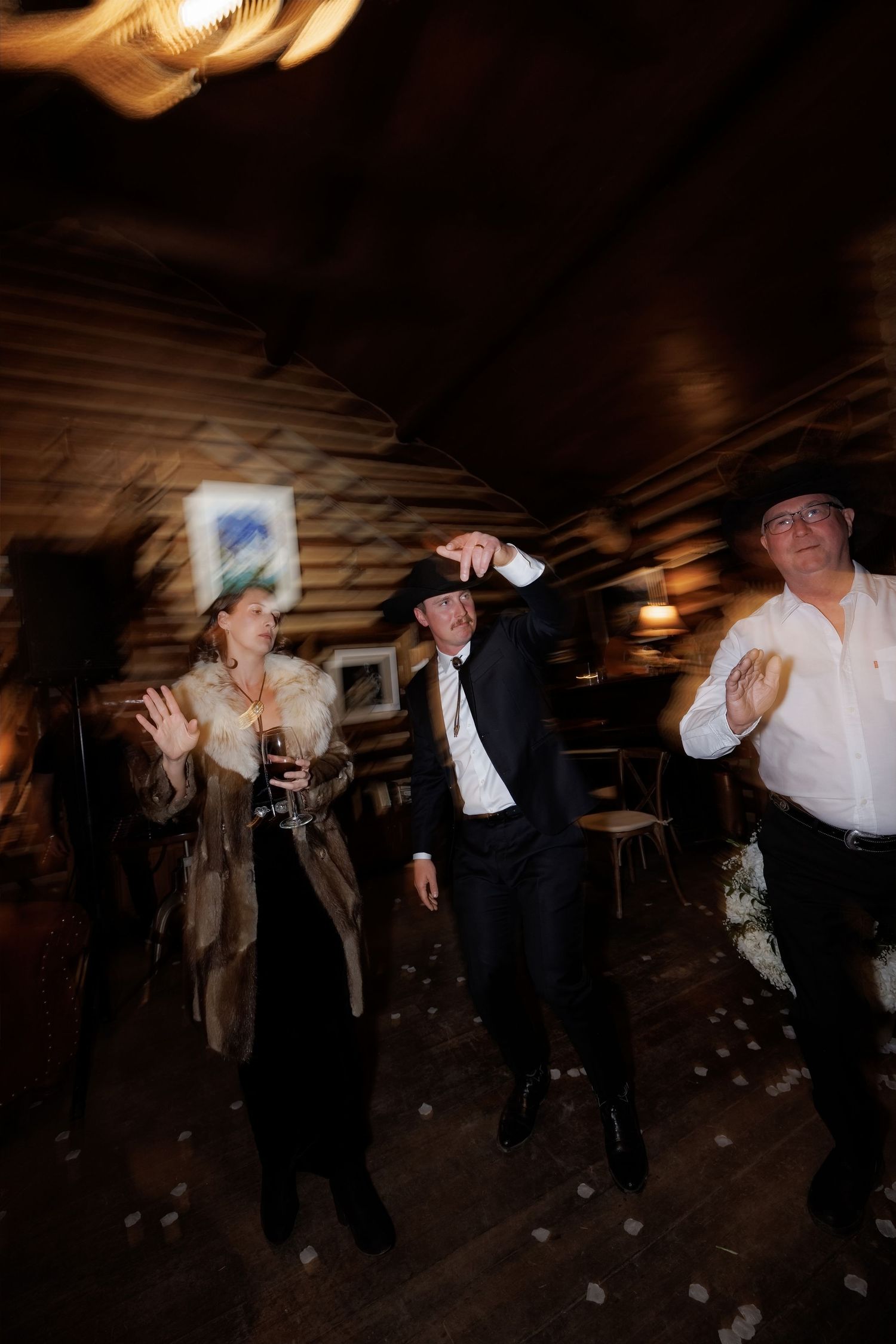 Guests dancing joyfully in a rustic log cabin wedding reception with warm ambient lighting.