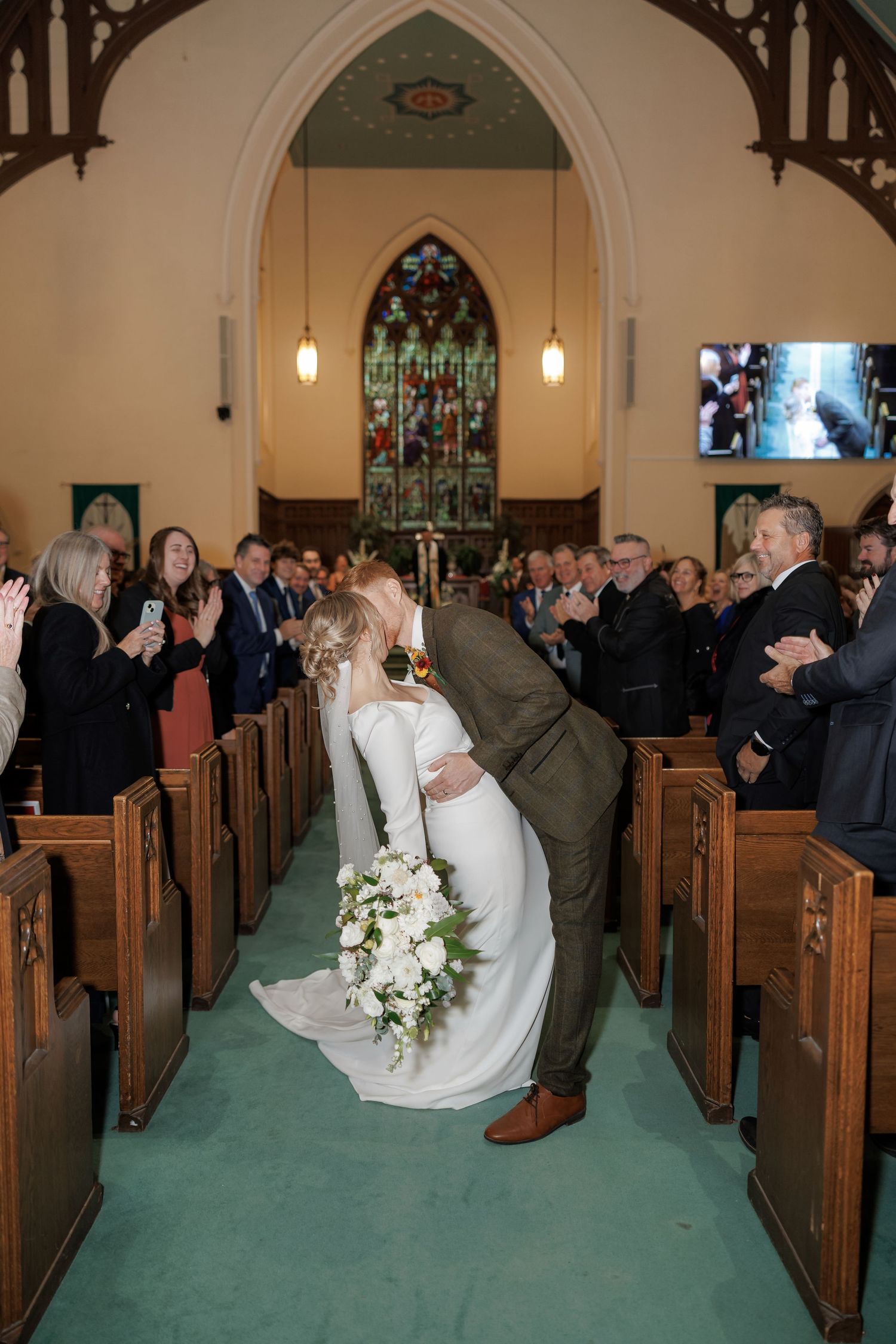 Wedding couple kneeling in church pews during ceremony while guests look on.