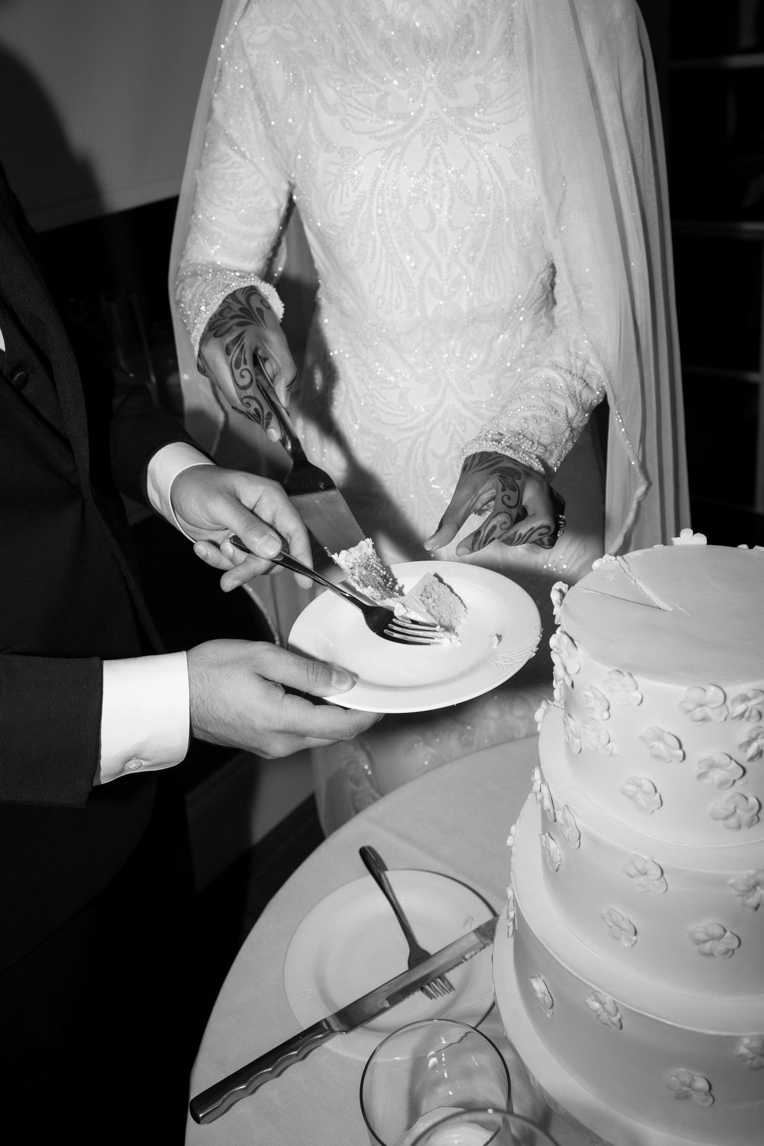Close-up of hands cutting an elegant white wedding cake with delicate floral details.