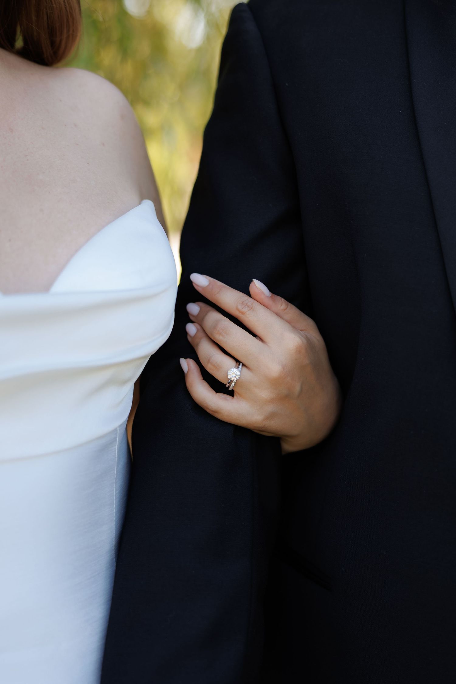 Elegant detail shot of a strapless white wedding dress against a black suit with ring.