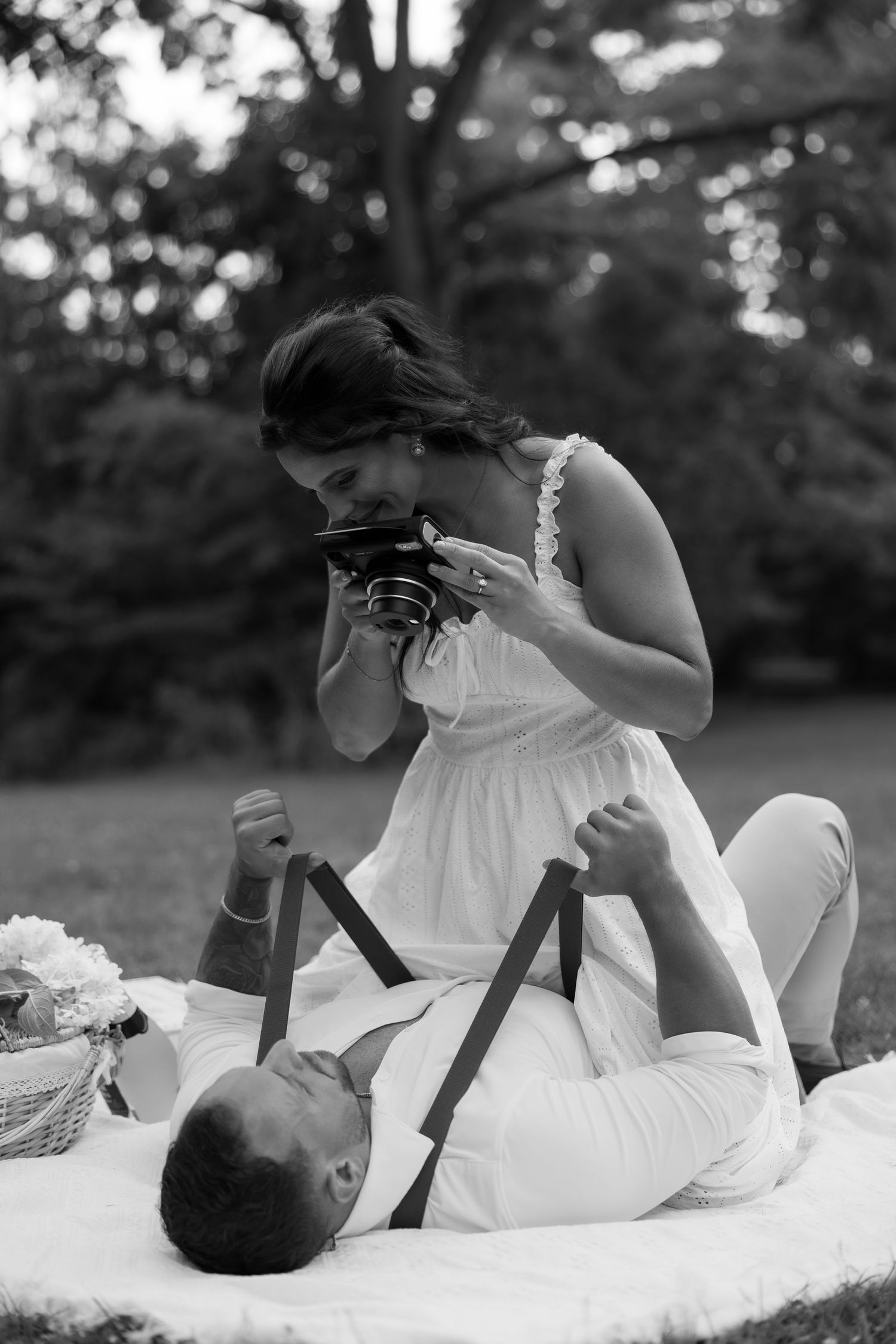 Black and white photo of couple lying on blanket taking pictures with vintage camera.