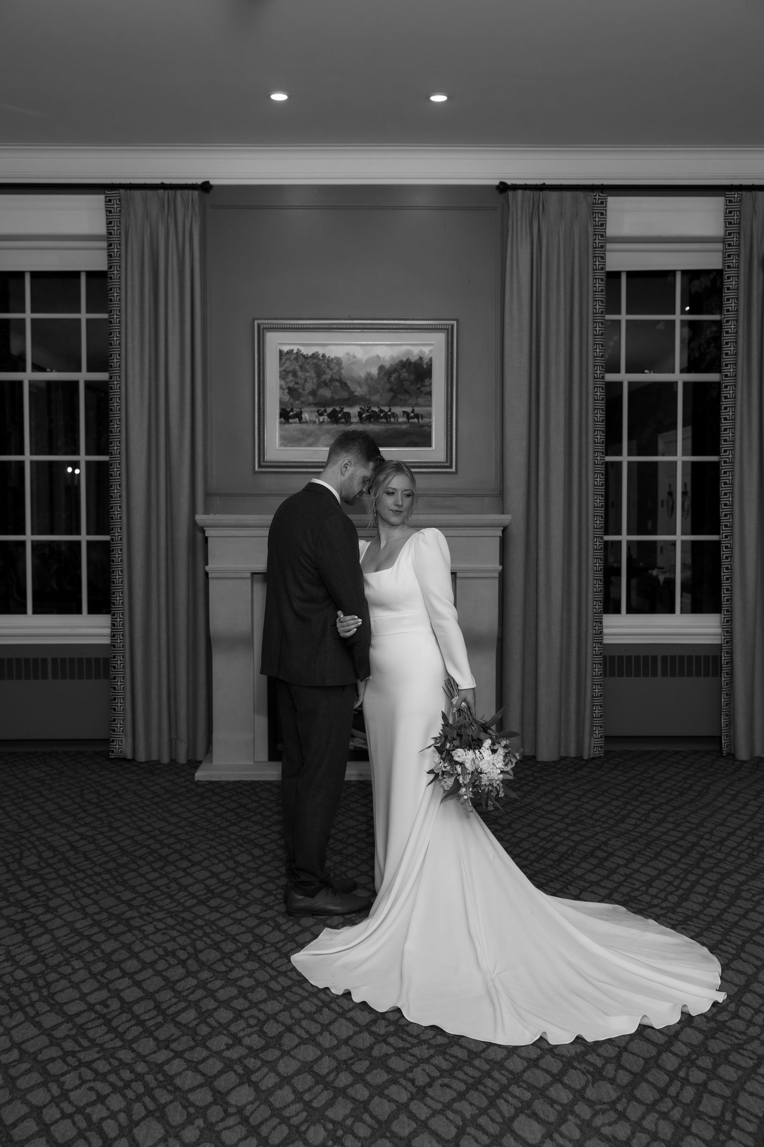 Black and white indoor wedding portraits show couple posing on patterned carpet in an elegant room.