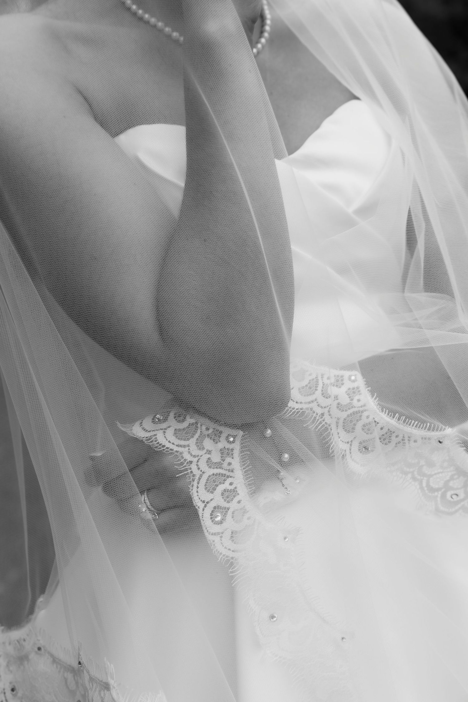 Black and white photo of a bride in a white strapless wedding gown with lace detail, veil, and pearl necklace.