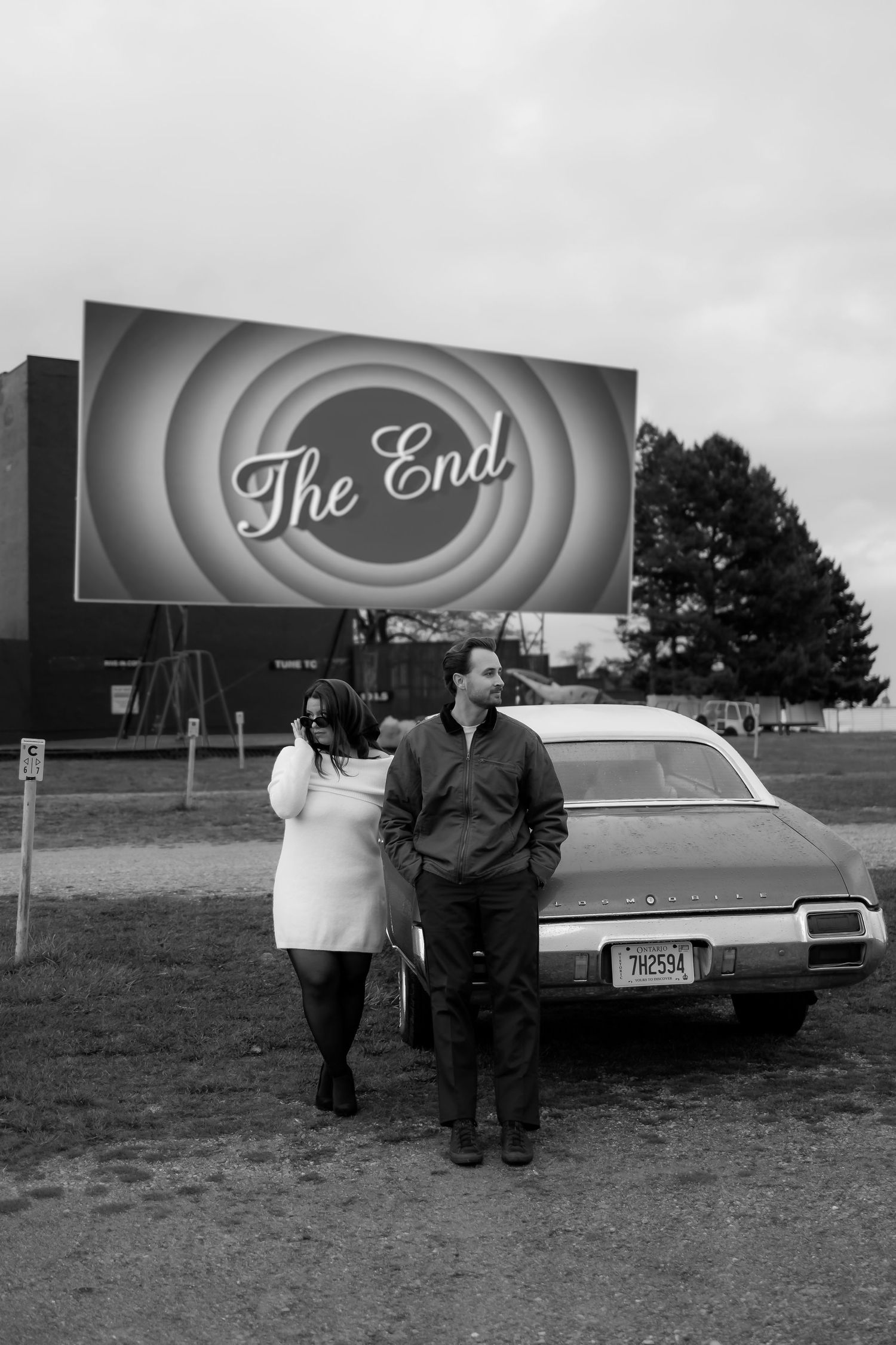 A retro drive-in movie screen displaying 'The End' with a vintage car parked beneath it in black and white.