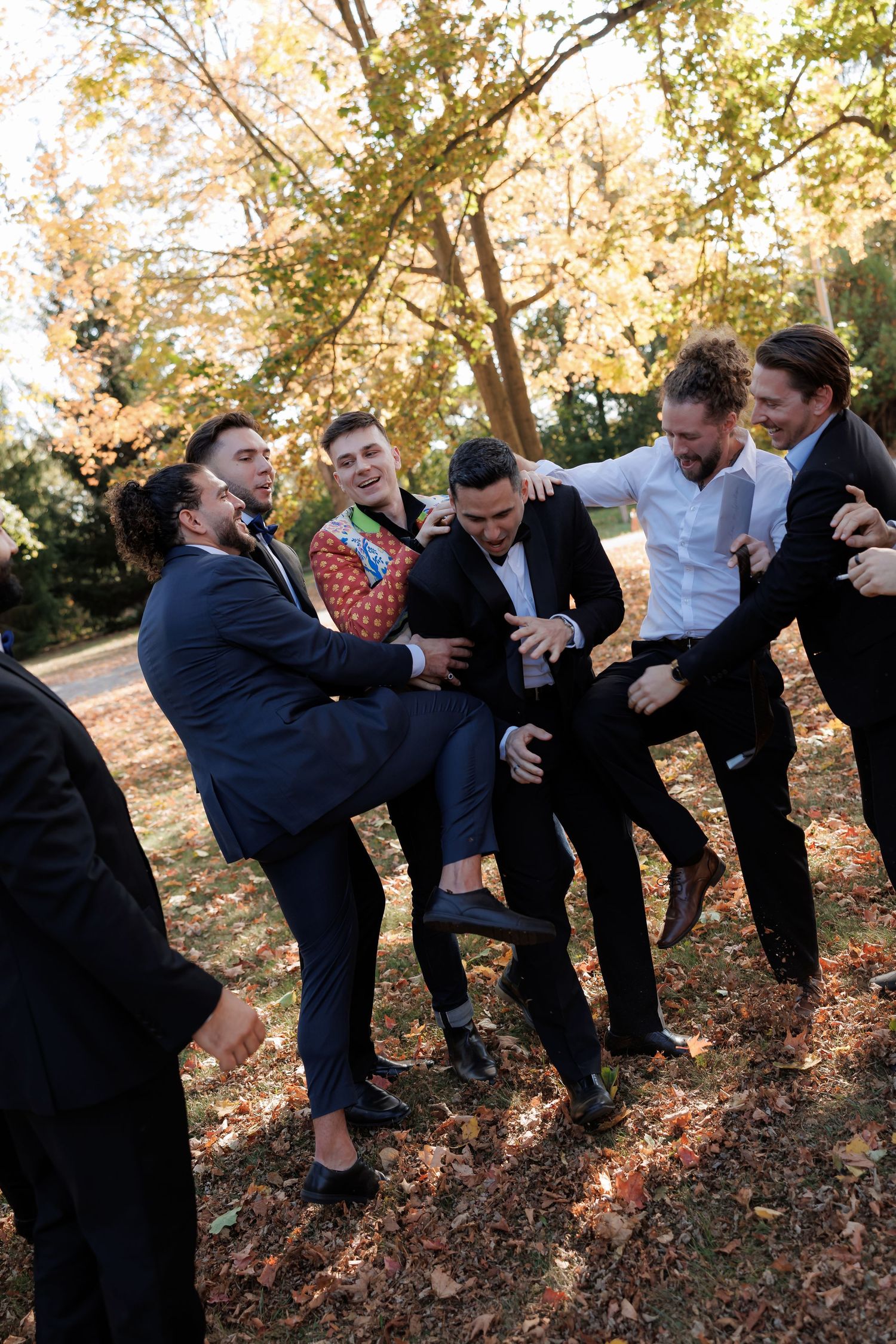 Groomsmen goofing around and posing playfully on autumn hillside.