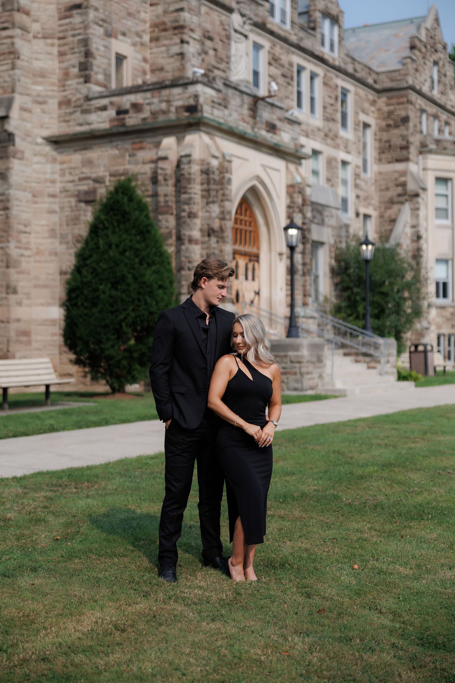Couple sharing a romantic moment on the lawn of a historic stone building.