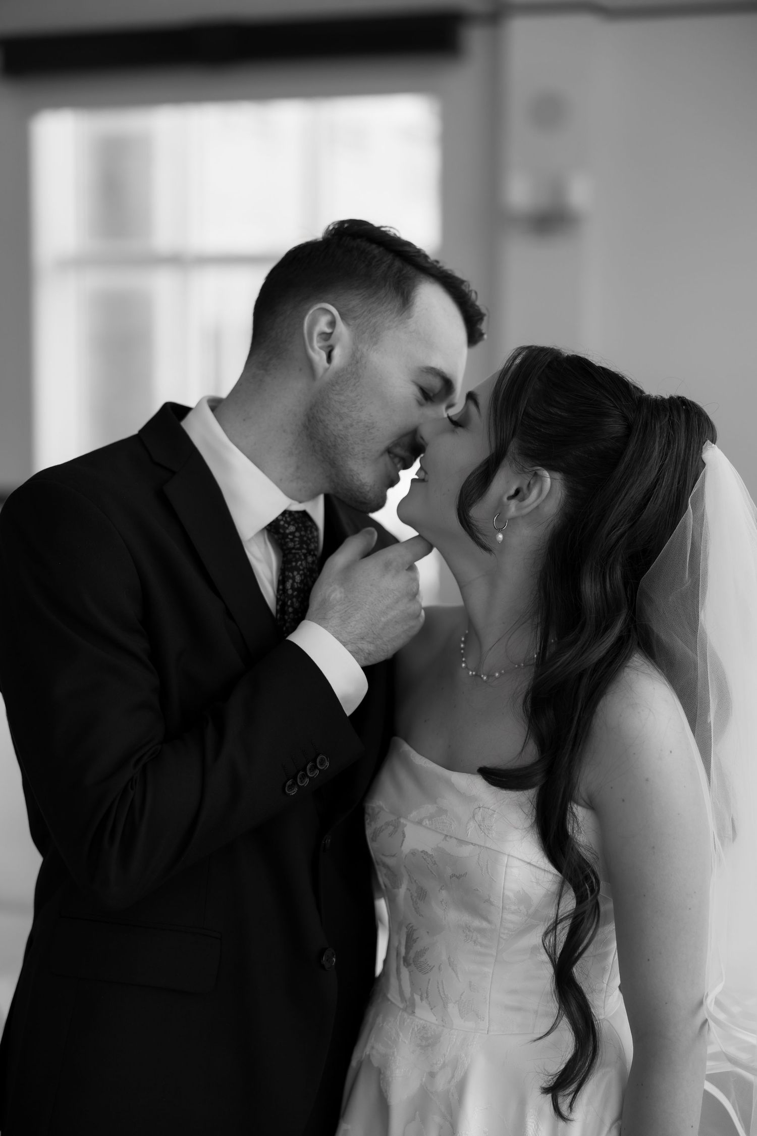Black and white photo of a bride and groom sharing a romantic kiss on their wedding day.