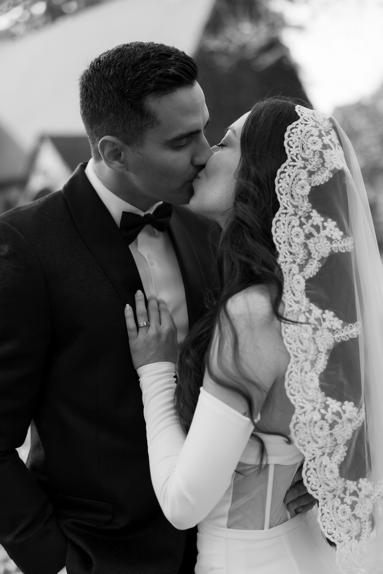 Intimate black and white portrait of newlyweds sharing a tender moment under lace veil.