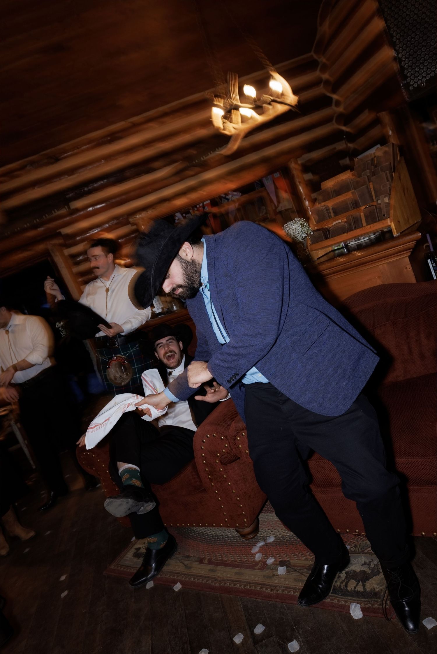 Men dancing energetically in a rustic wood-paneled room during a lively celebration or party event.