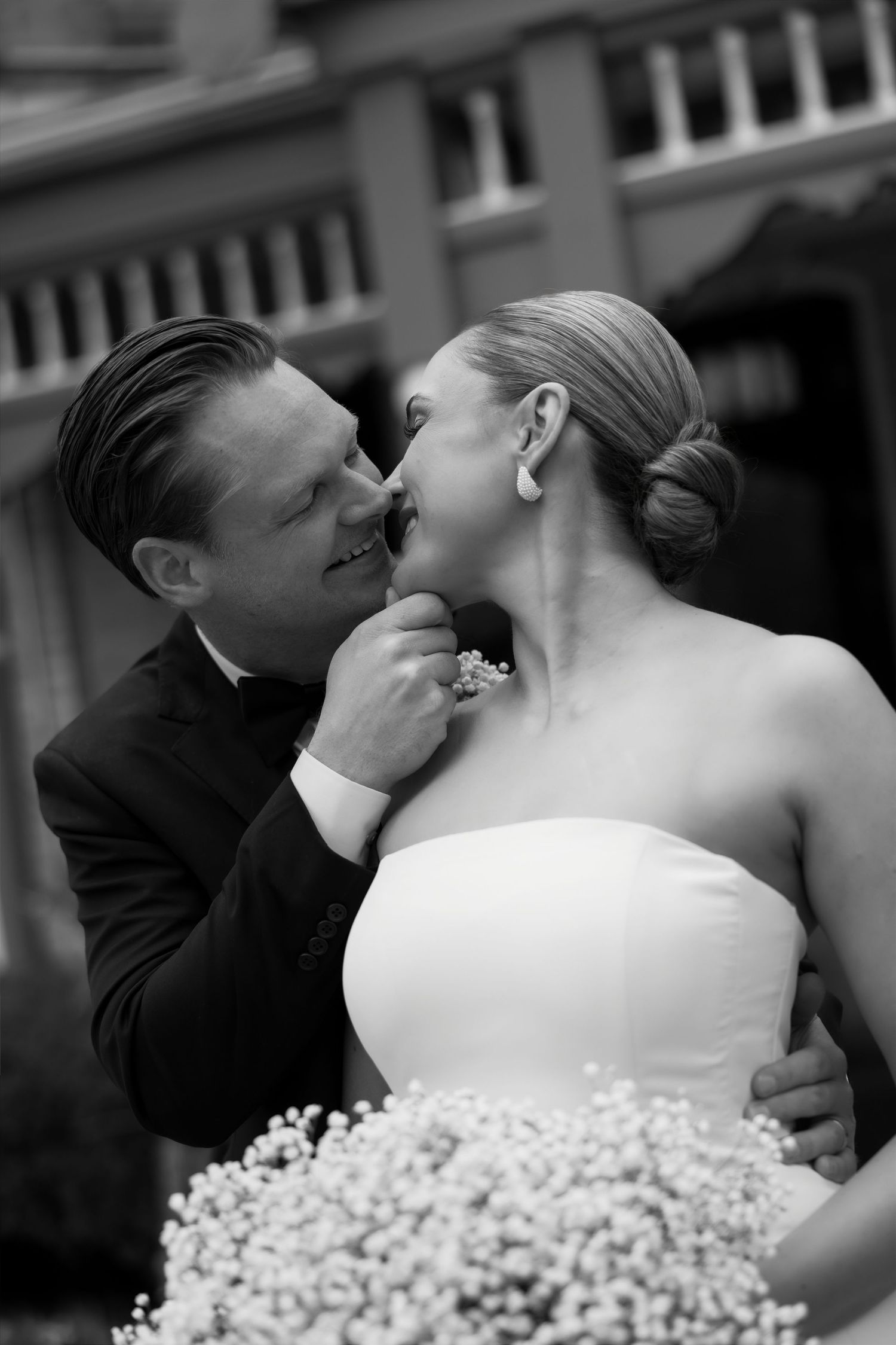 Groom tenderly touches brides chin as they share an intimate moment outdoors in classic black and white.