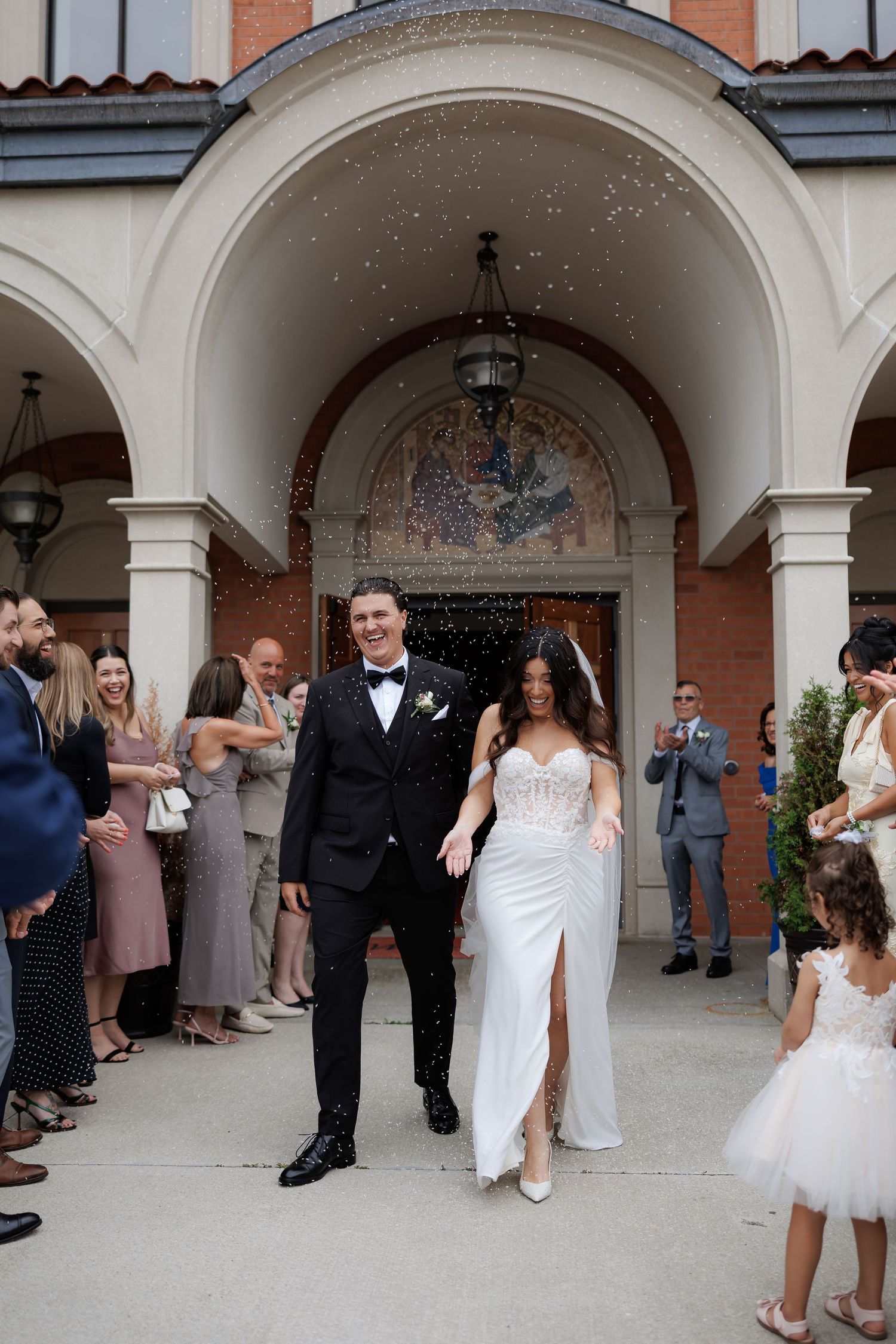 Wedding celebration under arched church entrance with guests throwing confetti.