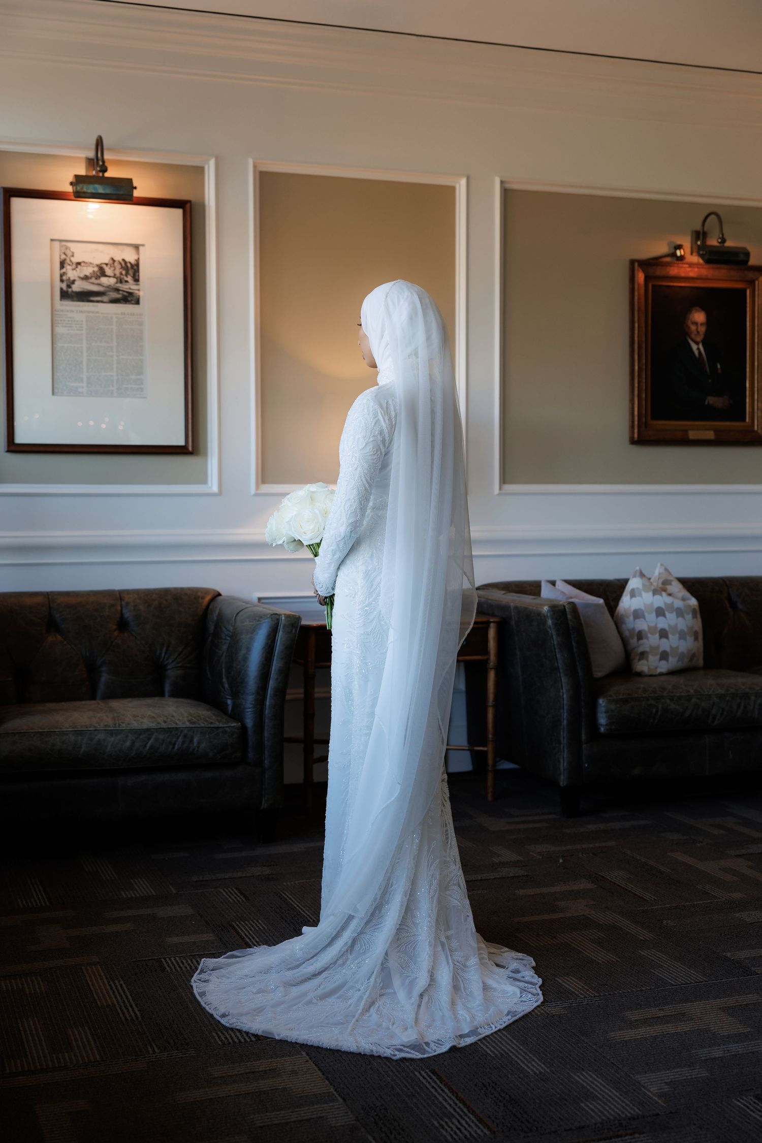 Elegant white wedding dress with a long train displayed in a room with framed artwork.