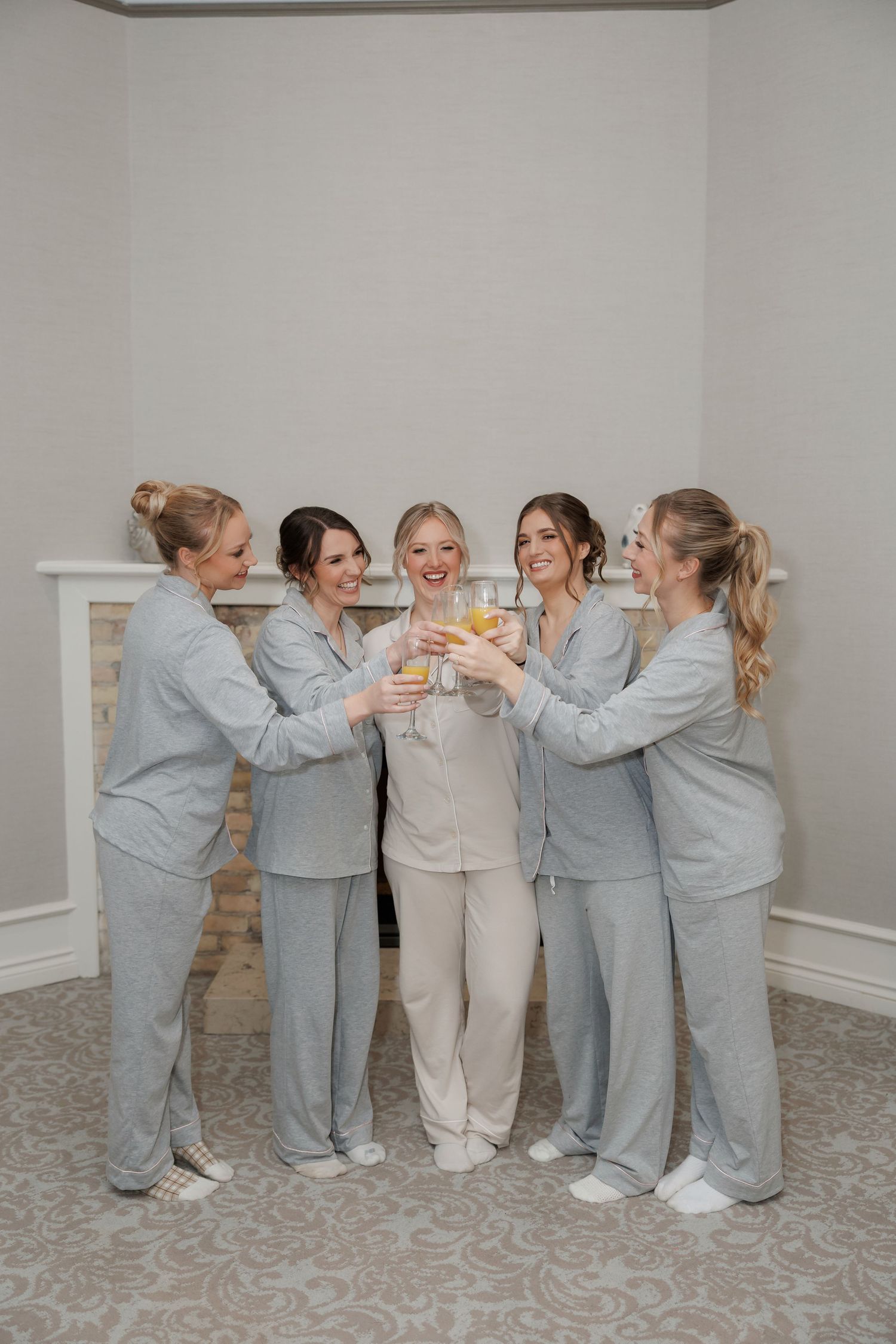 Bridesmaids in matching gray loungewear toast together during wedding preparations.