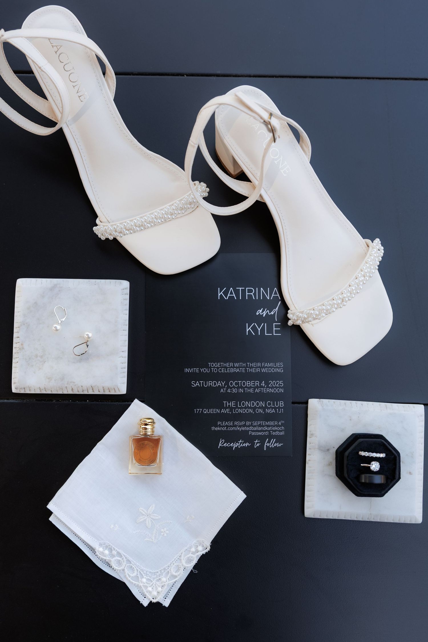 Wedding accessories including white shoes, invitations and perfume arranged on dark background.