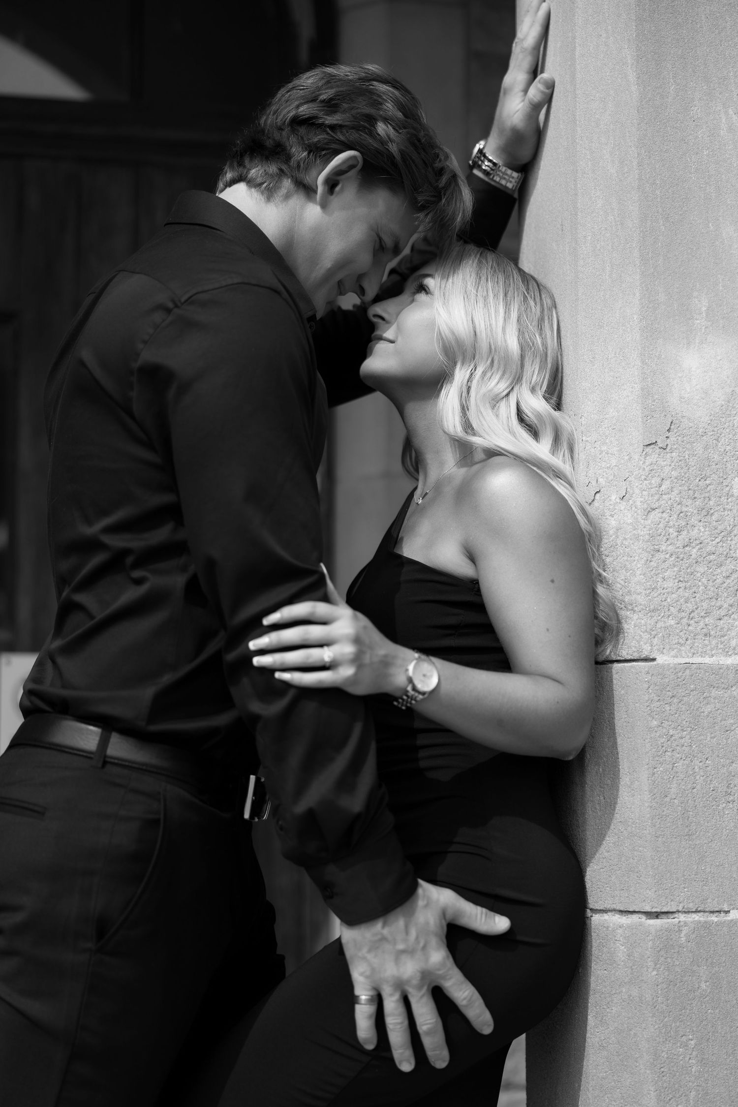 Romantic black and white photo of a couple in formal attire embracing against a wall.
