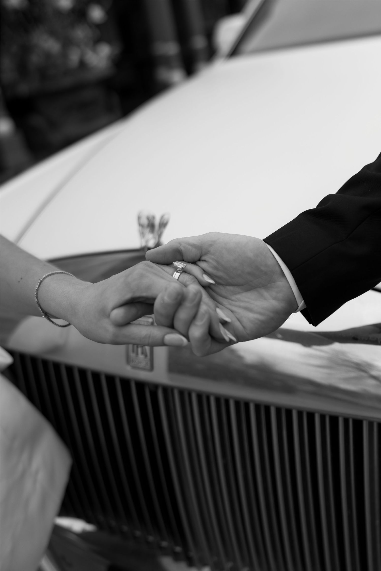 Black and white photo of groom placing wedding ring on bride's finger in front of a Rolls-Royce car.