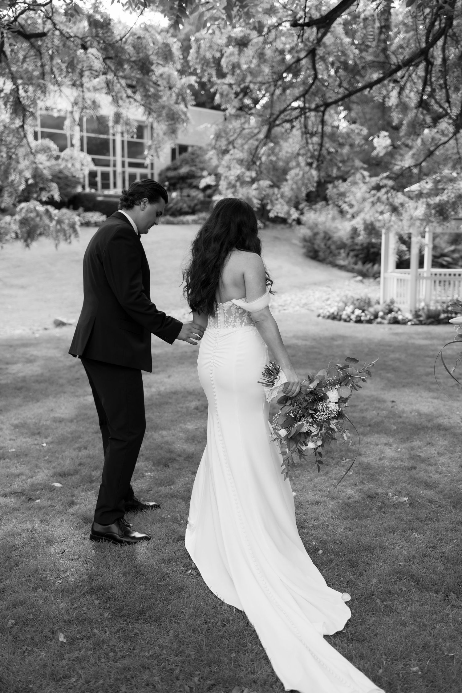 Black and white photo of wedding couple walking on garden lawn.