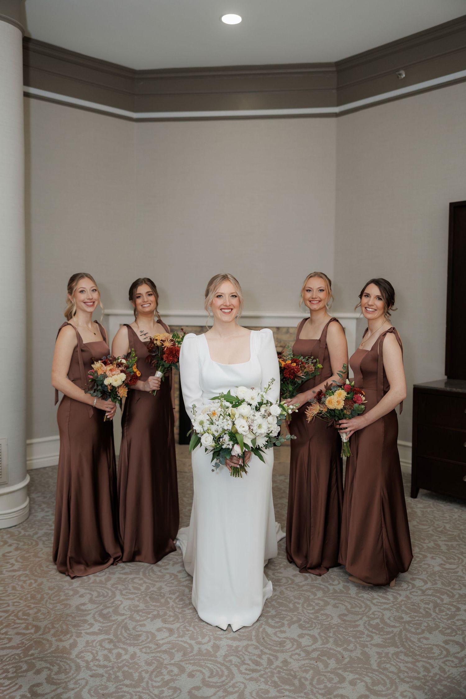 Bridal party in chocolate brown dresses poses with white wedding gown.
