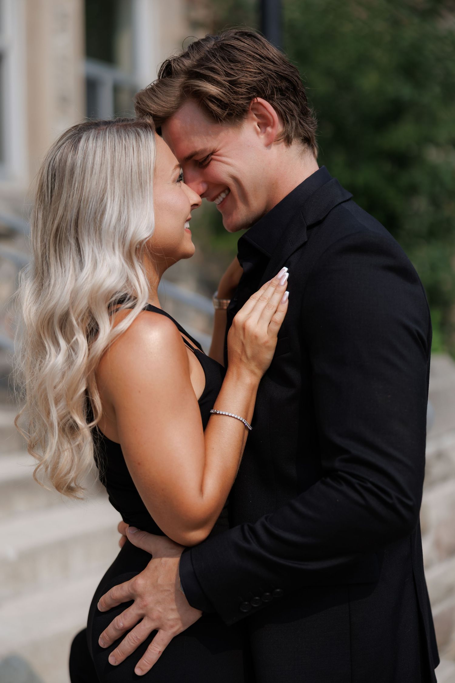 Intimate portrait of a couple in black sharing a romantic moment against stone architecture.