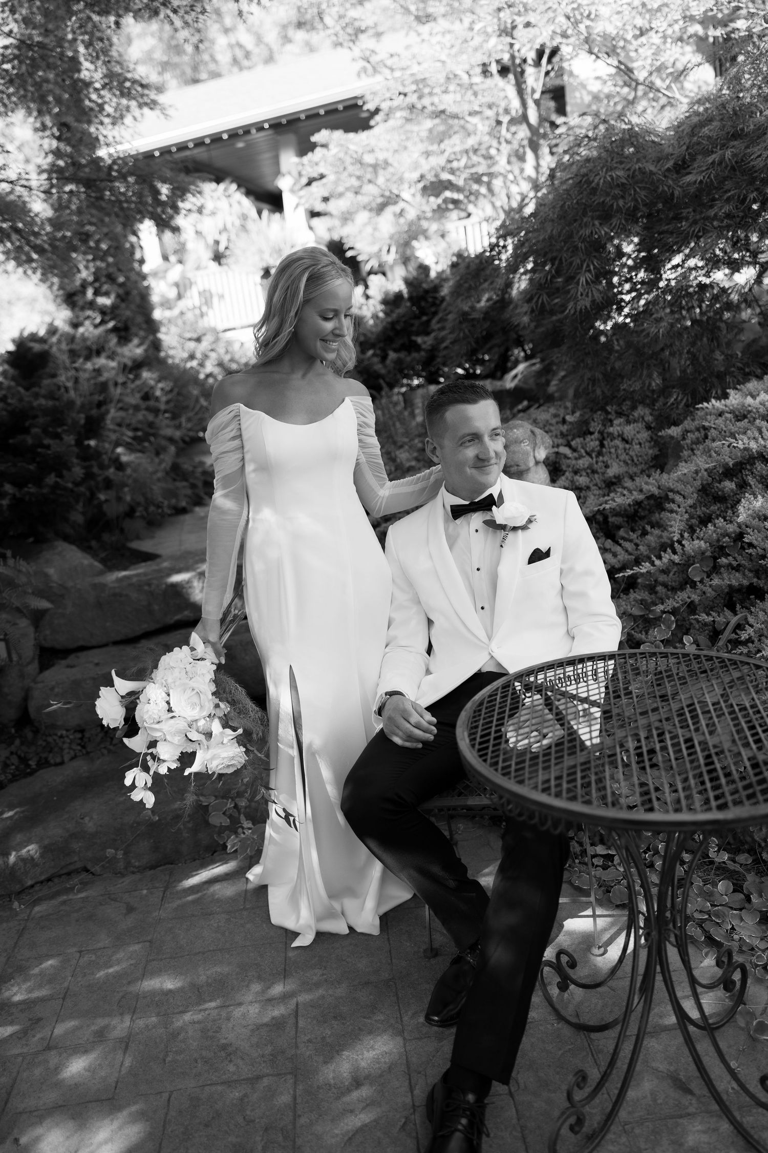 Black and white photo of a couple sharing intimate moments near a decorative garden bench.