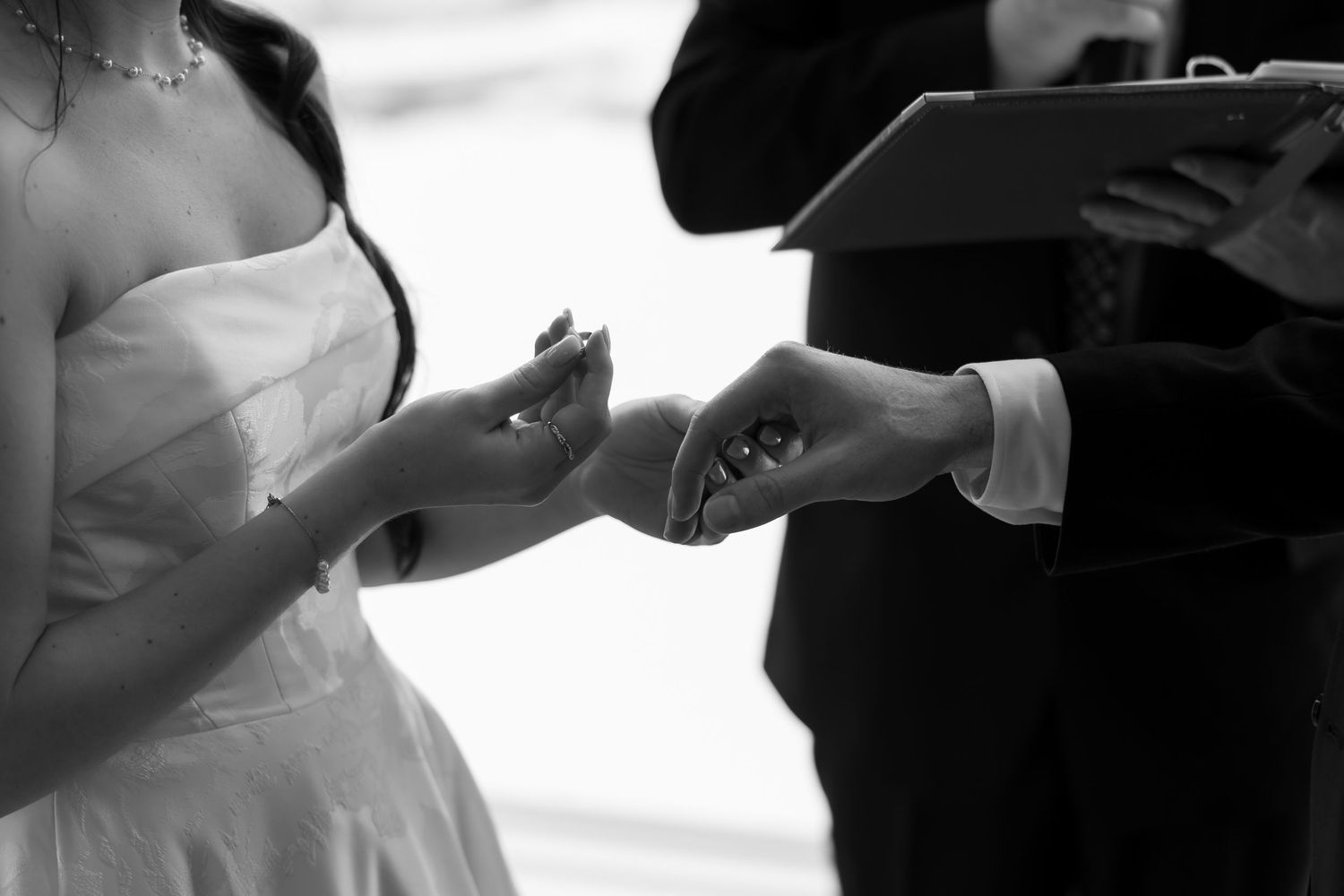 Black and white photo of bride and groom exchanging wedding rings during ceremony.