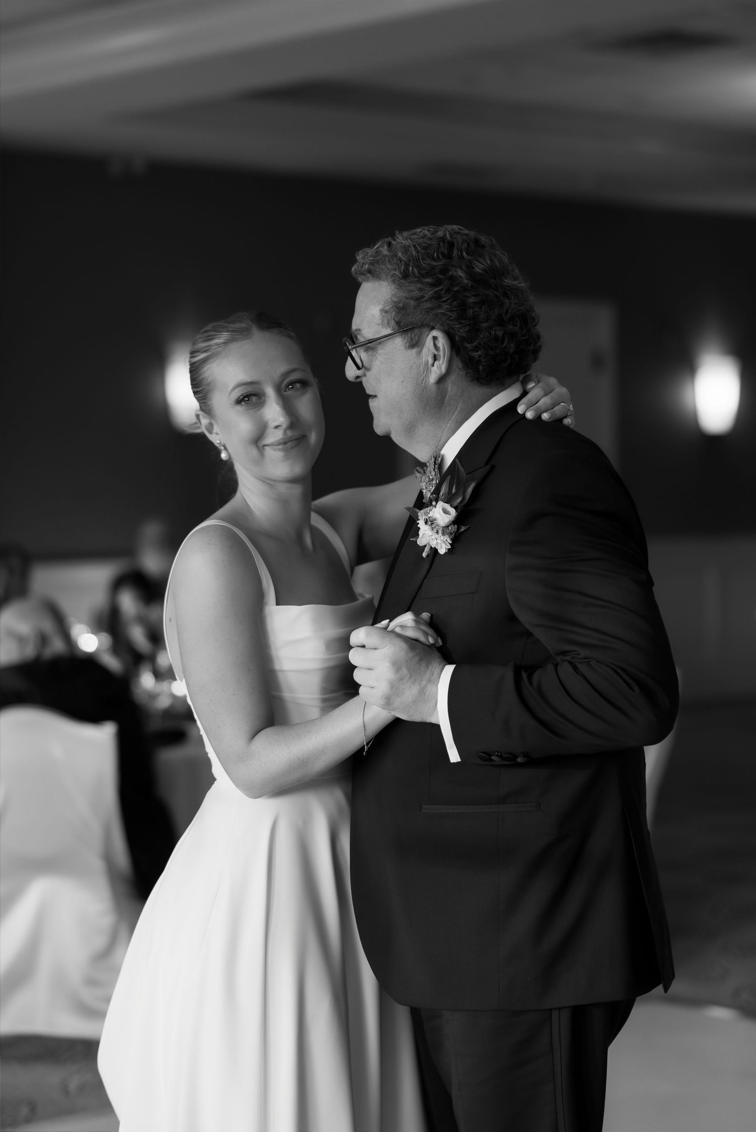 Black and white photo of bride sharing emotional father-daughter dance at wedding reception.