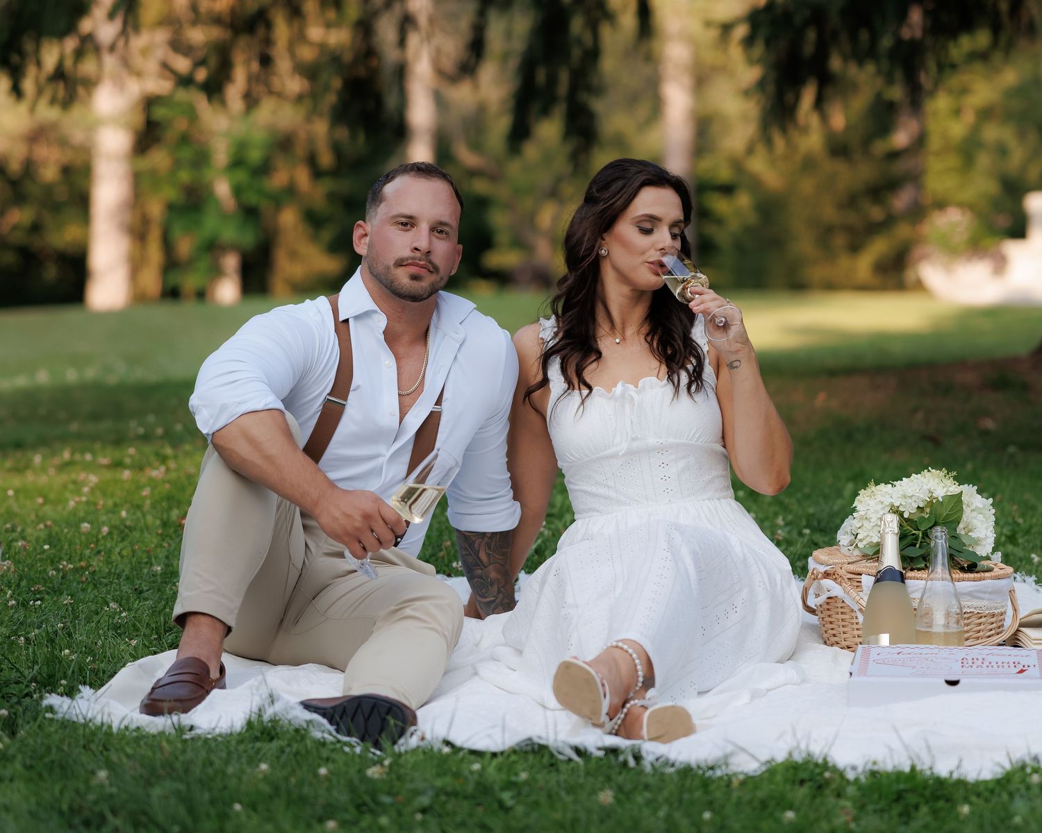 Romantic outdoor picnic scene with couple in white clothing relaxing on blanket.