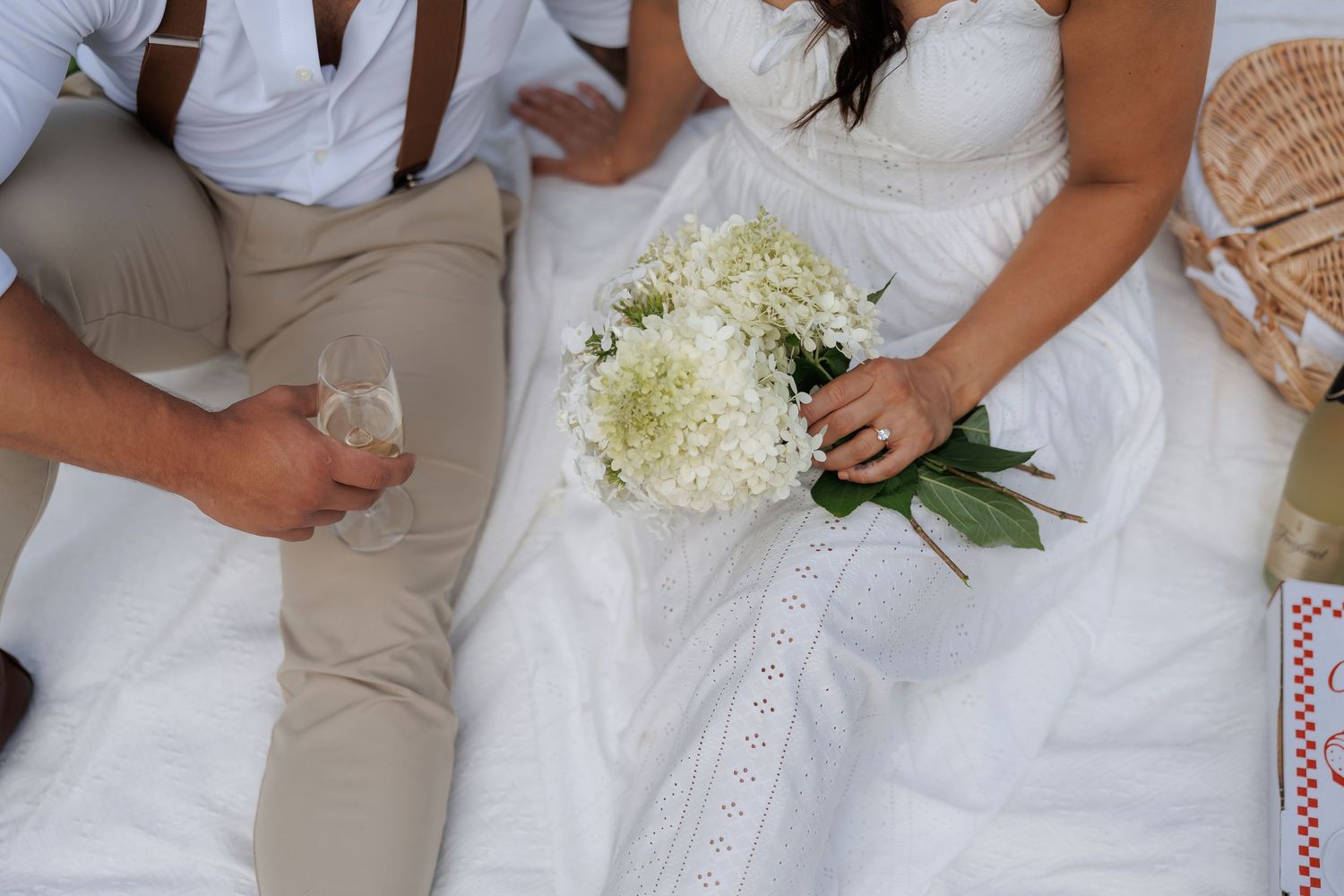 Wedding party members in white dresses and khaki suits hold bouquets while standing together in a formal group photo.