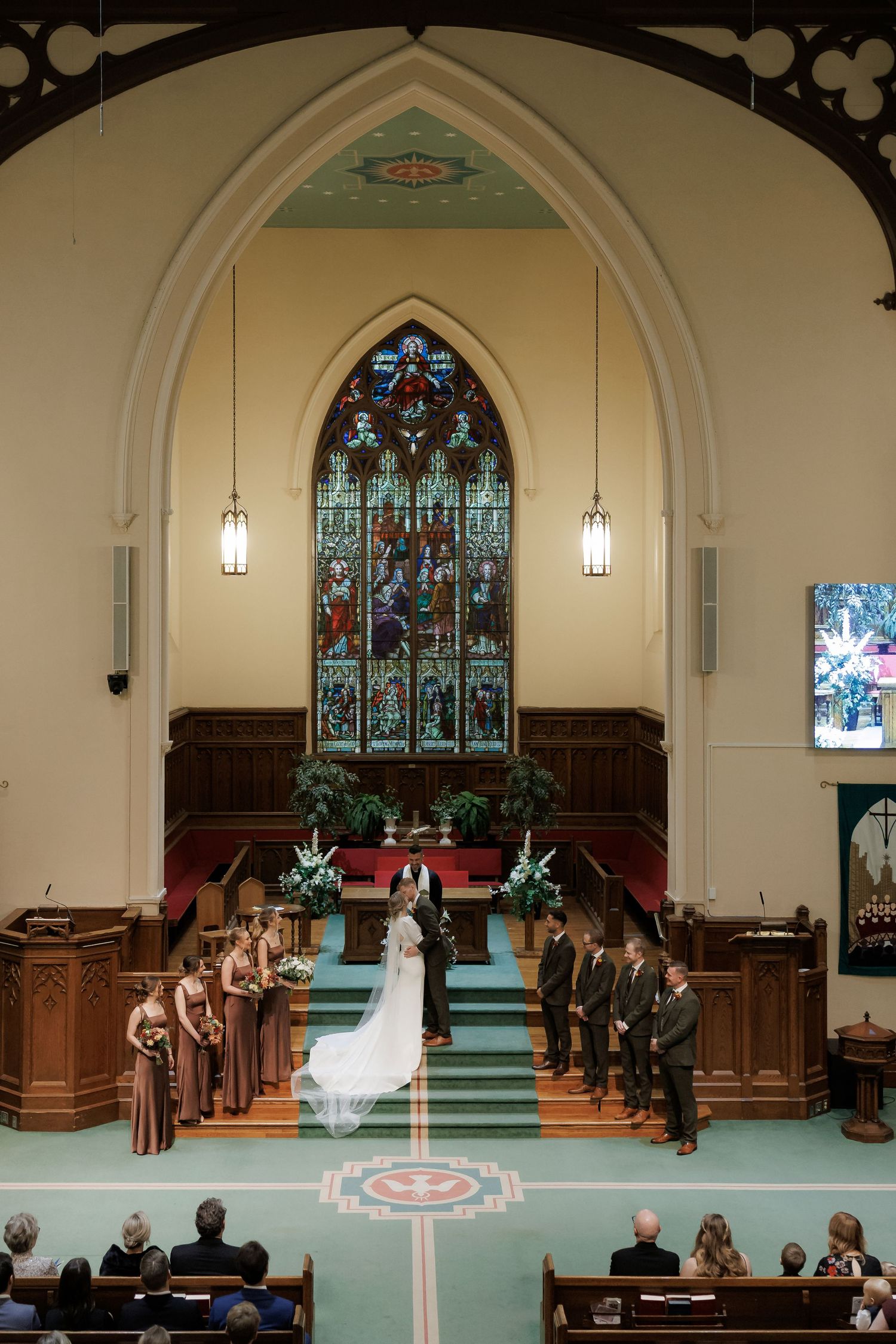 Traditional church ceremony with green carpet aisle and stained glass windows in background.