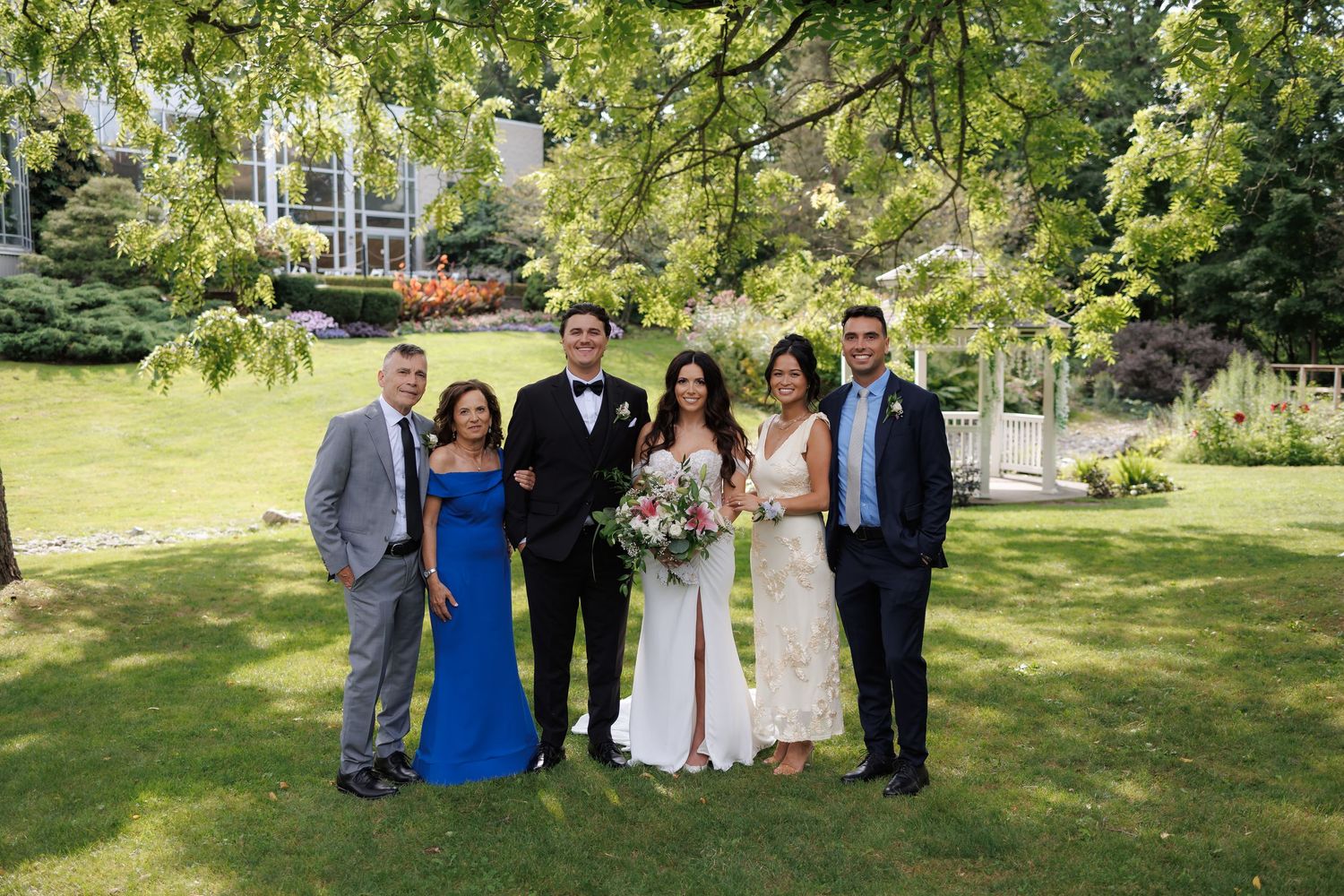 Wedding party gathered on a sunny lawn for group photos.