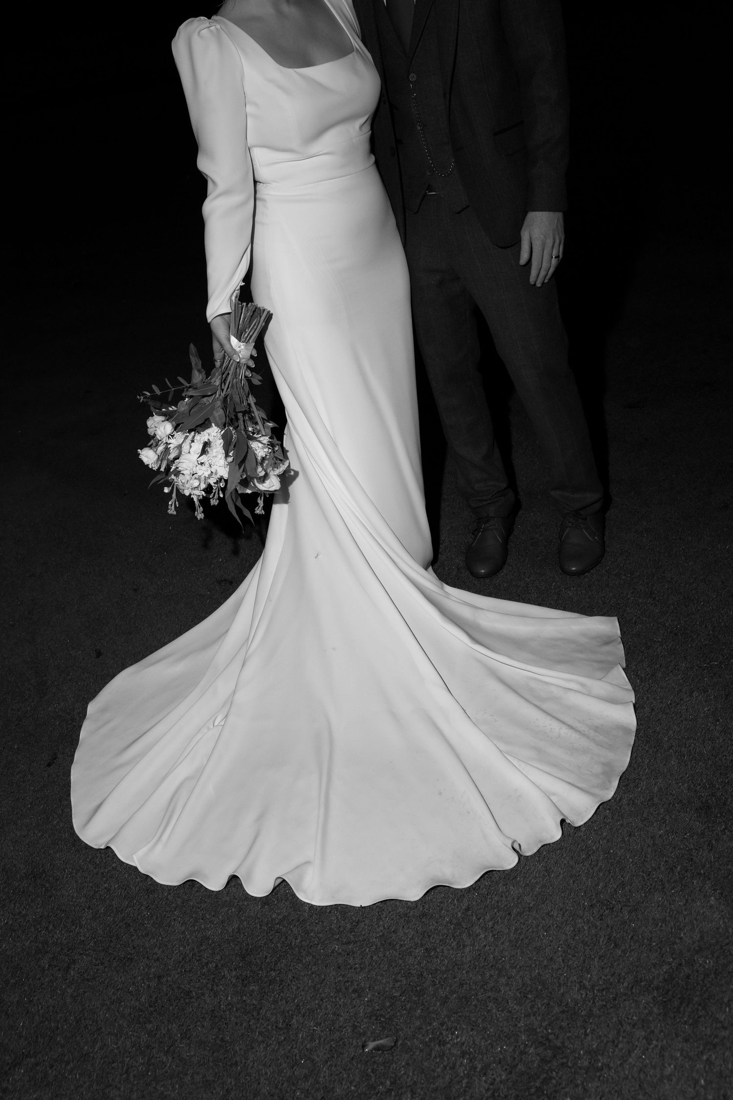 Elegant flowing white wedding dress details captured in dramatic black and white photography.