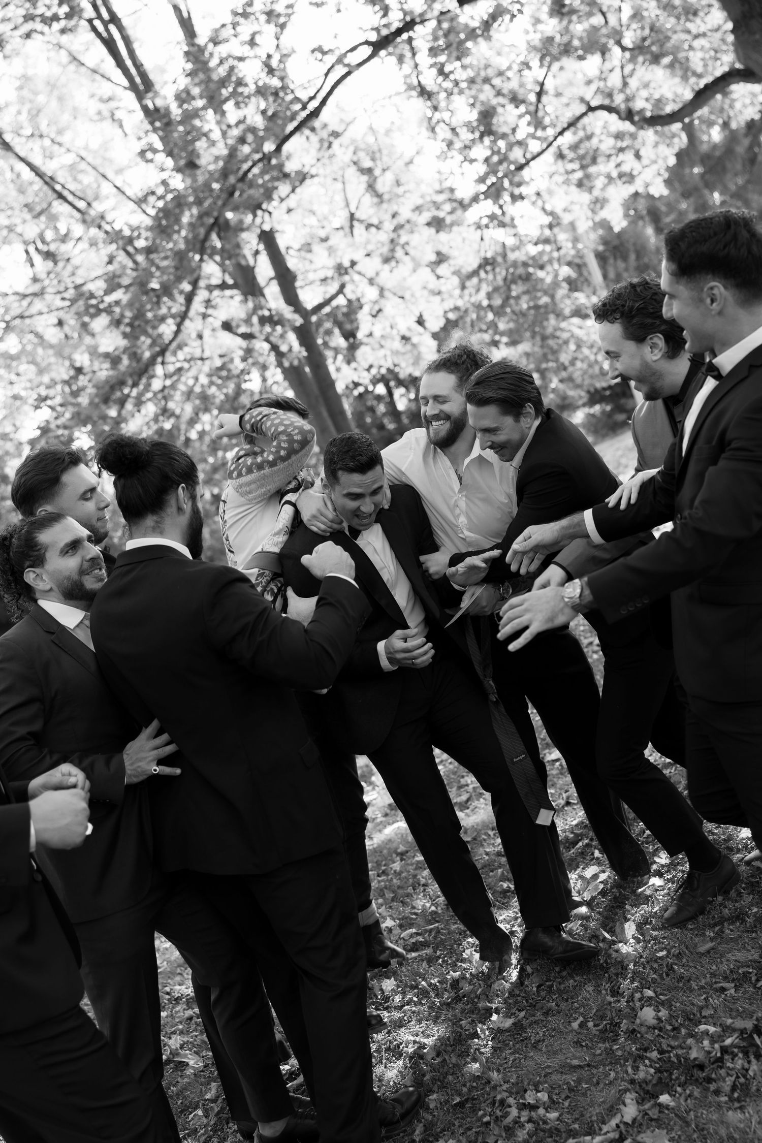 Black and white photo of groomsmen sharing candid moment outdoors.