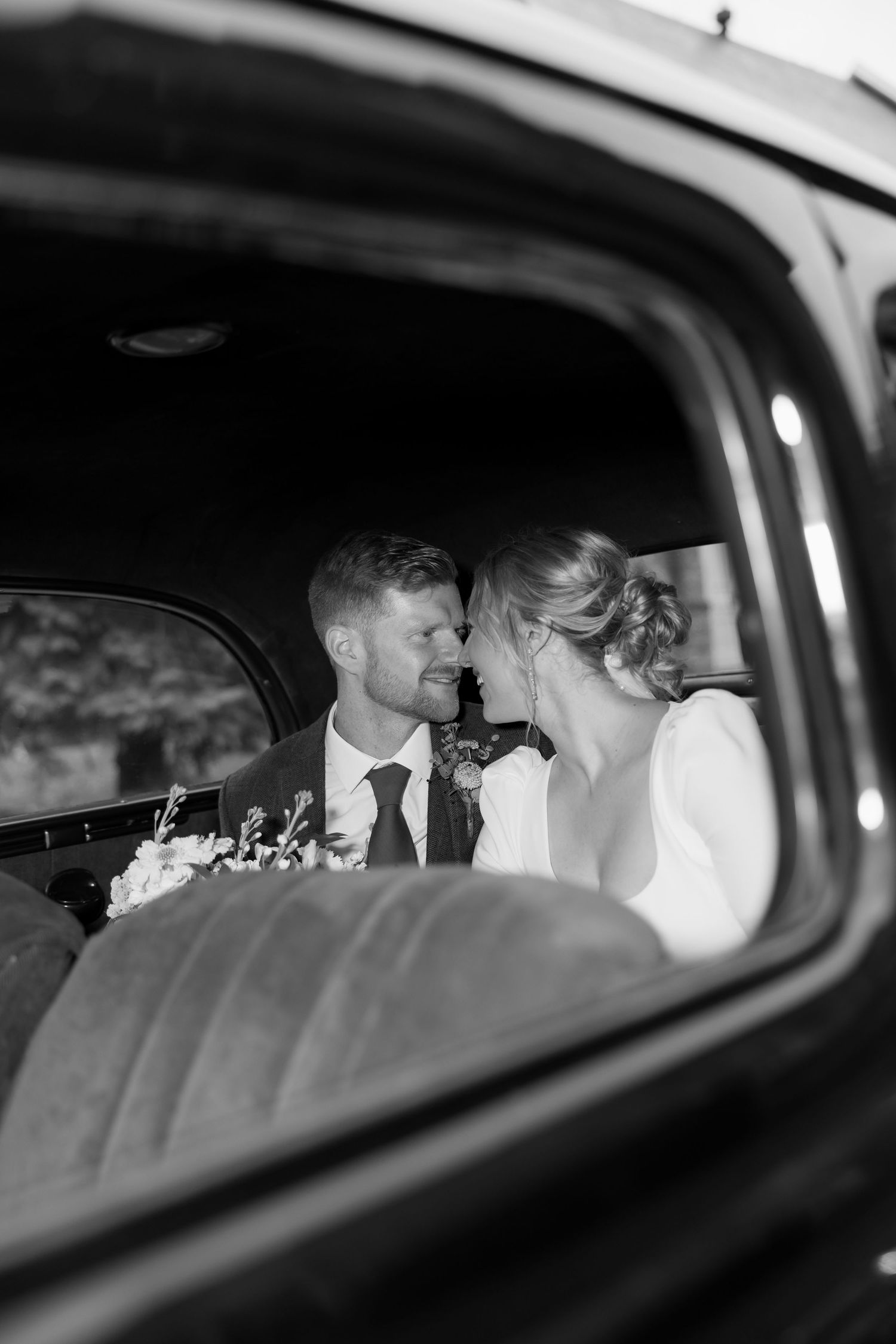 A romantic black and white photo of a couple sharing an intimate moment in the backseat of a vintage car.