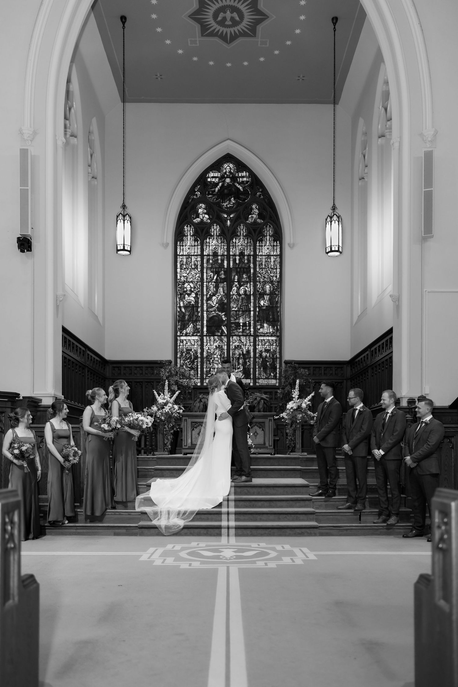 Church wedding ceremony with guests seated in pews under ornate stained glass windows.
