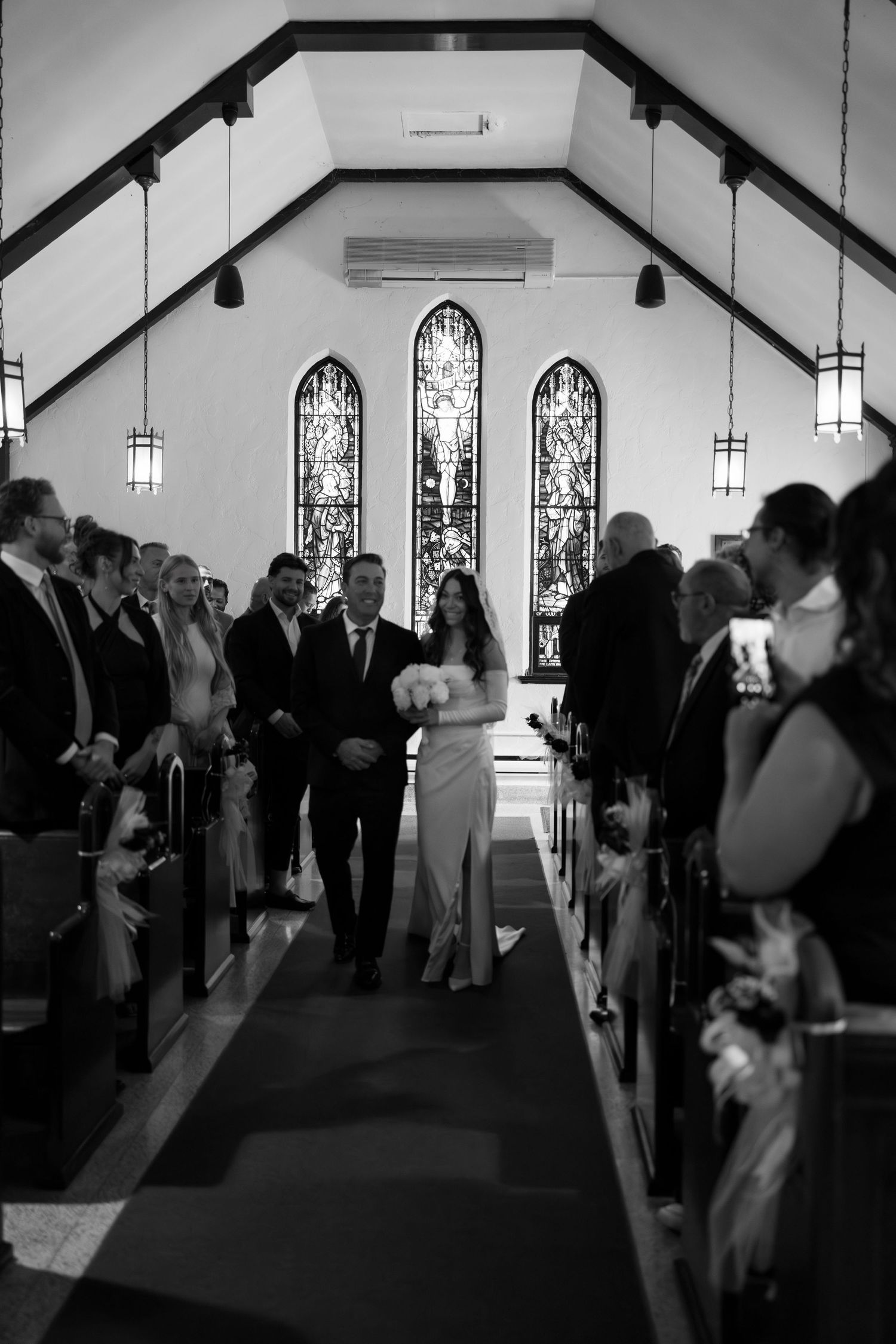 Wedding guests gather in church sanctuary with stained glass windows and vaulted ceiling.