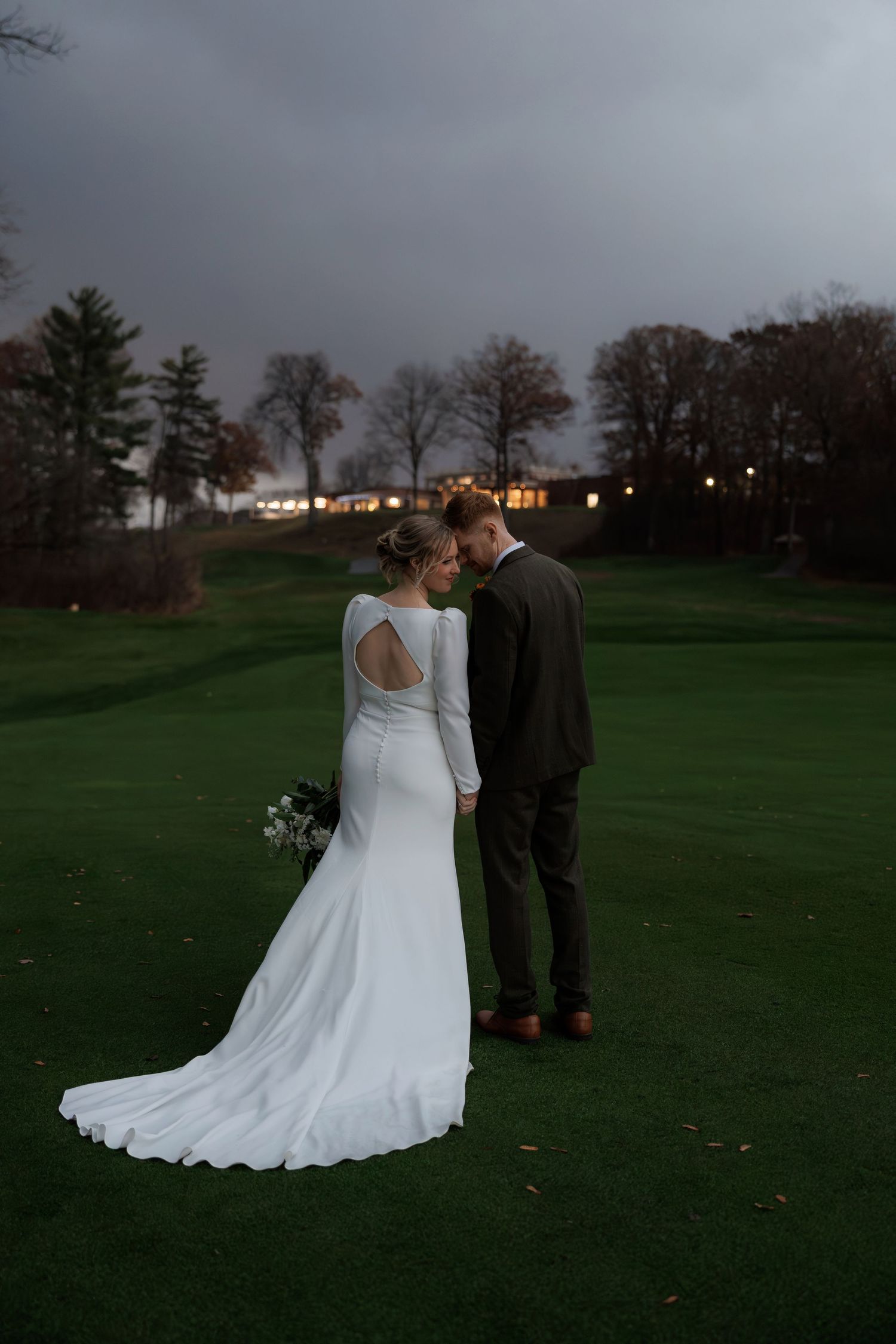 Wedding couple poses together on a grassy hill under dramatic overcast skies.