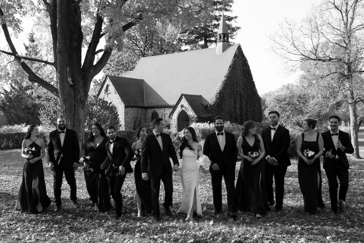 Black and white photo of wedding party arranged in creative poses outdoors.