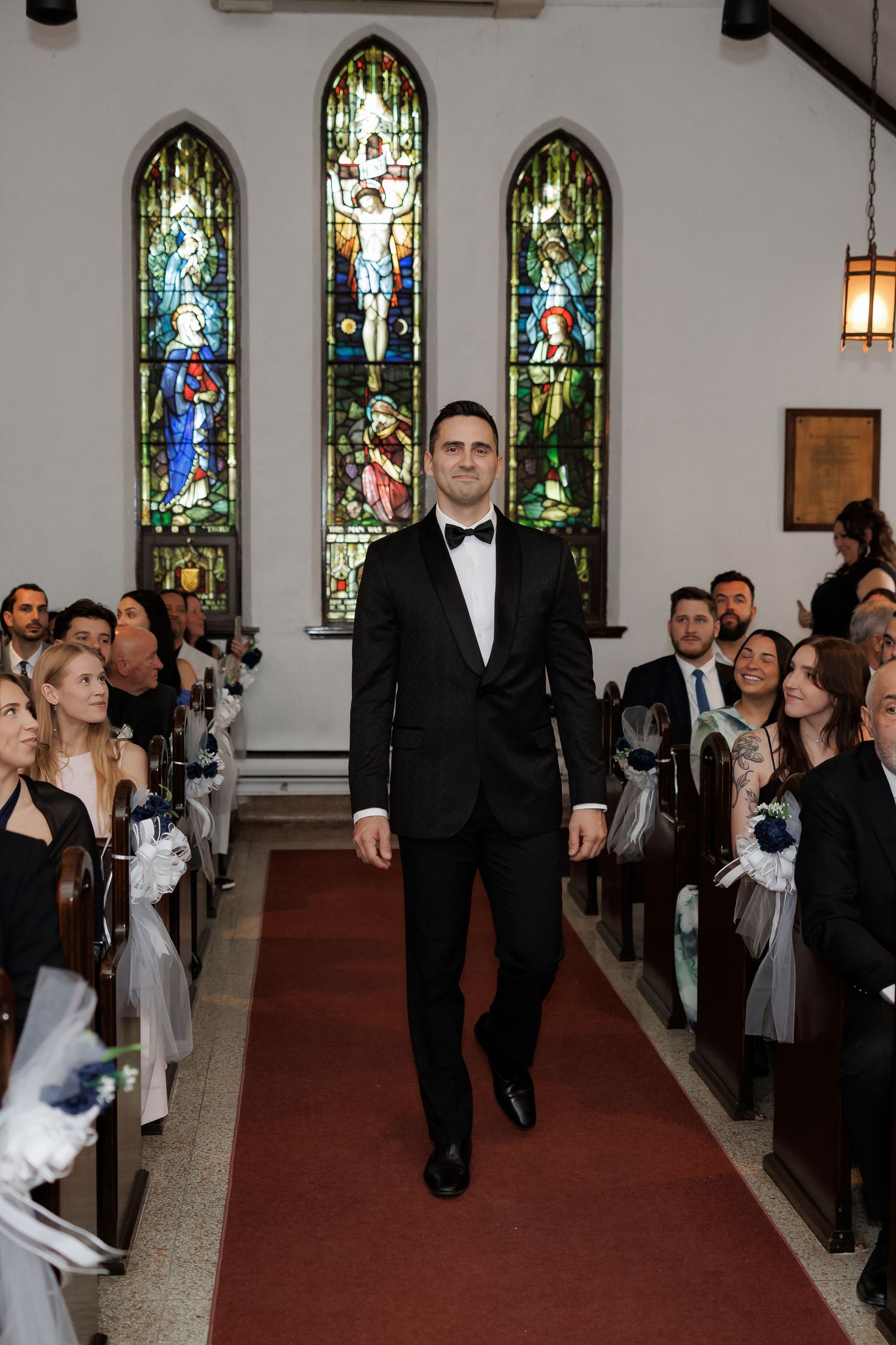 Wedding ceremony processional in church aisle with stained glass windows.