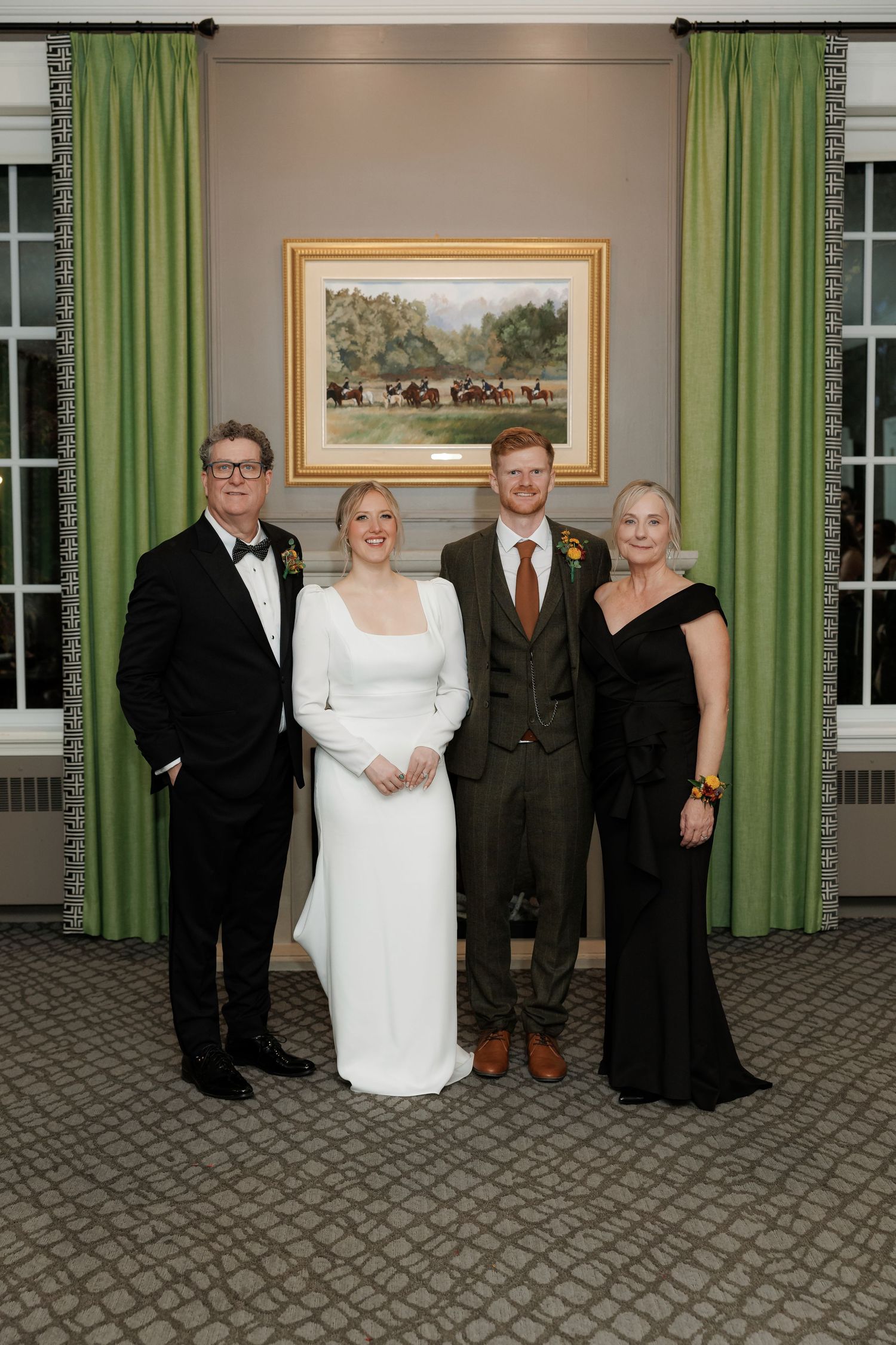 Wedding party poses in formal attire against green curtains in an elegant indoor setting.