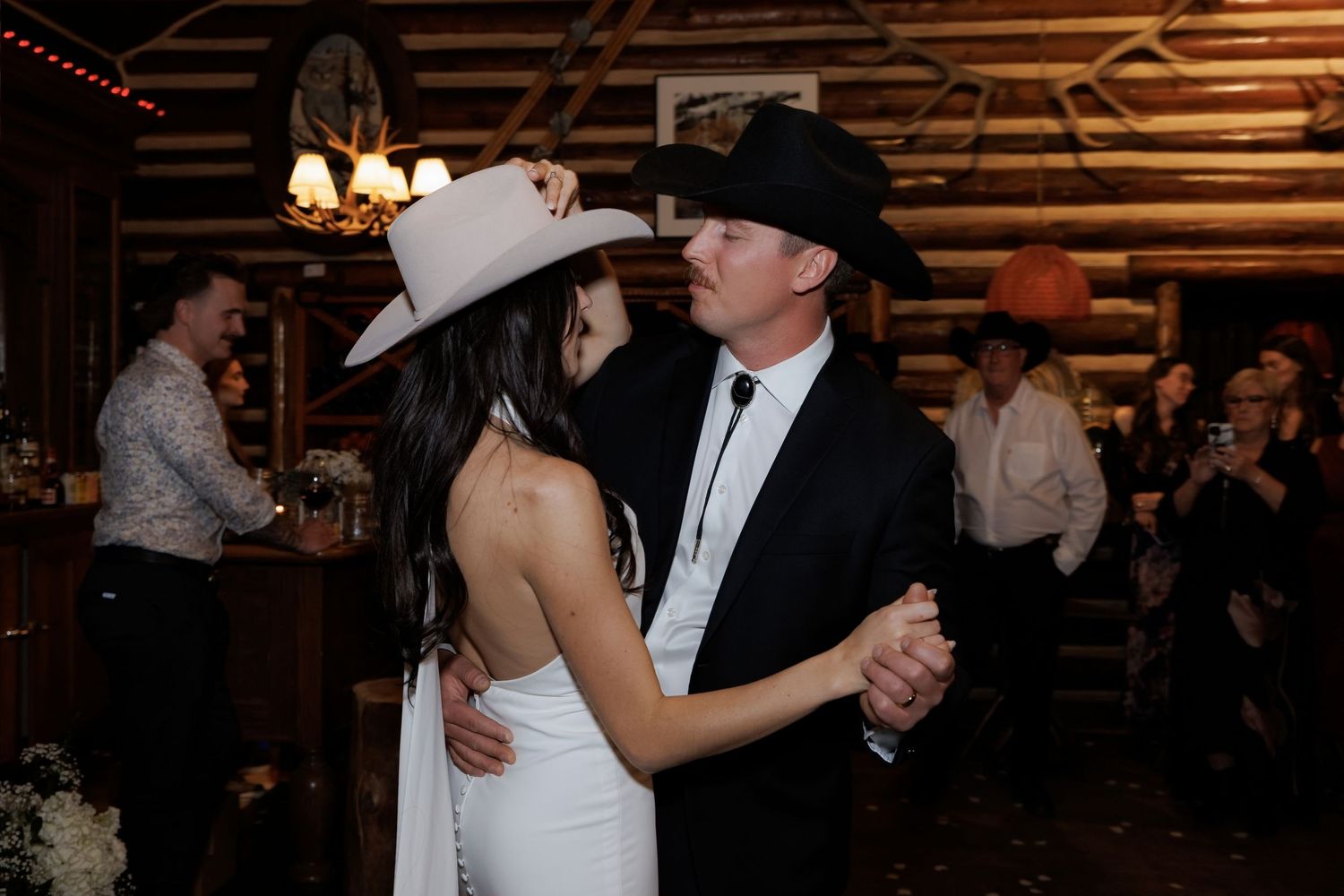 Bride and groom share first dance in cowboy hats at a rustic log cabin wedding venue.